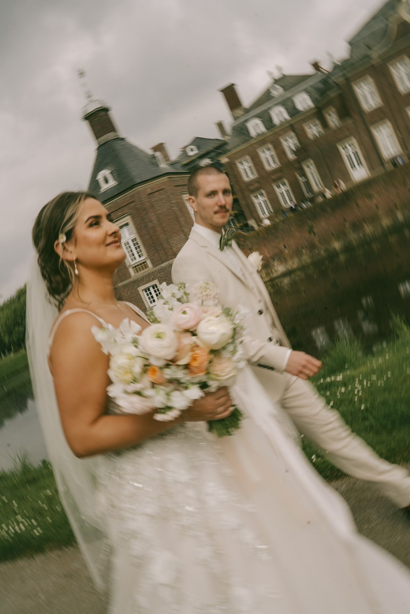 Couple in wedding attire walking past a grand historic Castle in Germany with bouquet in hand.