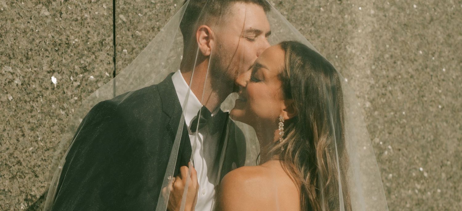 Romantic wedding couple sharing an intimate moment against a textured stone wall.