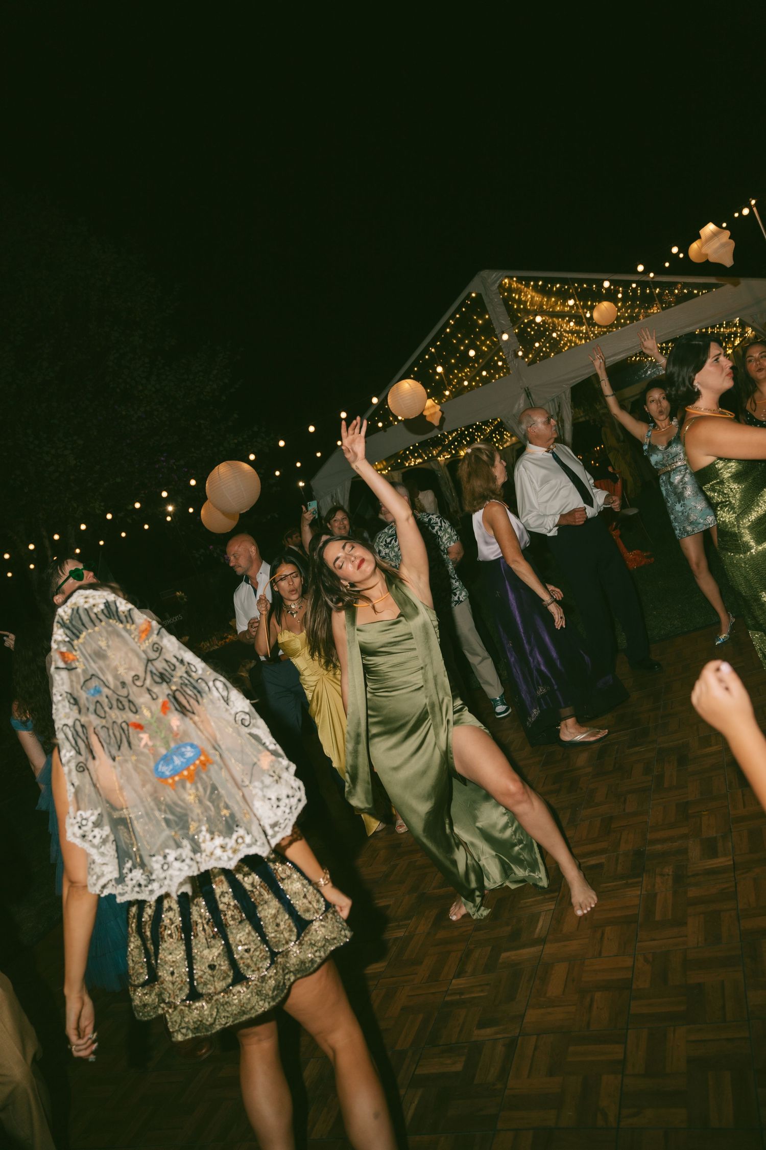 People dancing and celebrating at a nighttime party under string lights on a wooden floor.