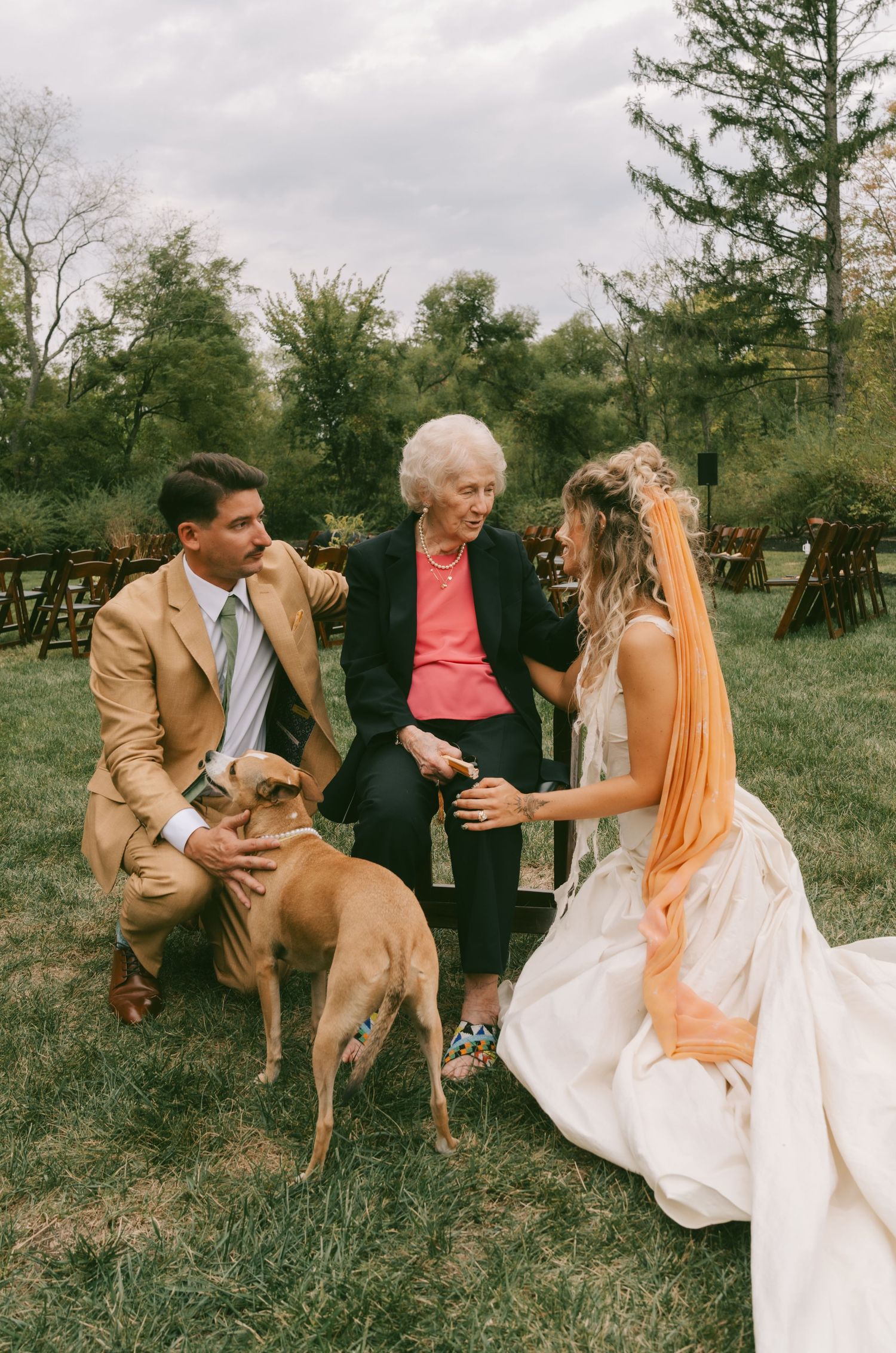 Wedding party members in formal attire dancing and laughing together on a grassy lawn.