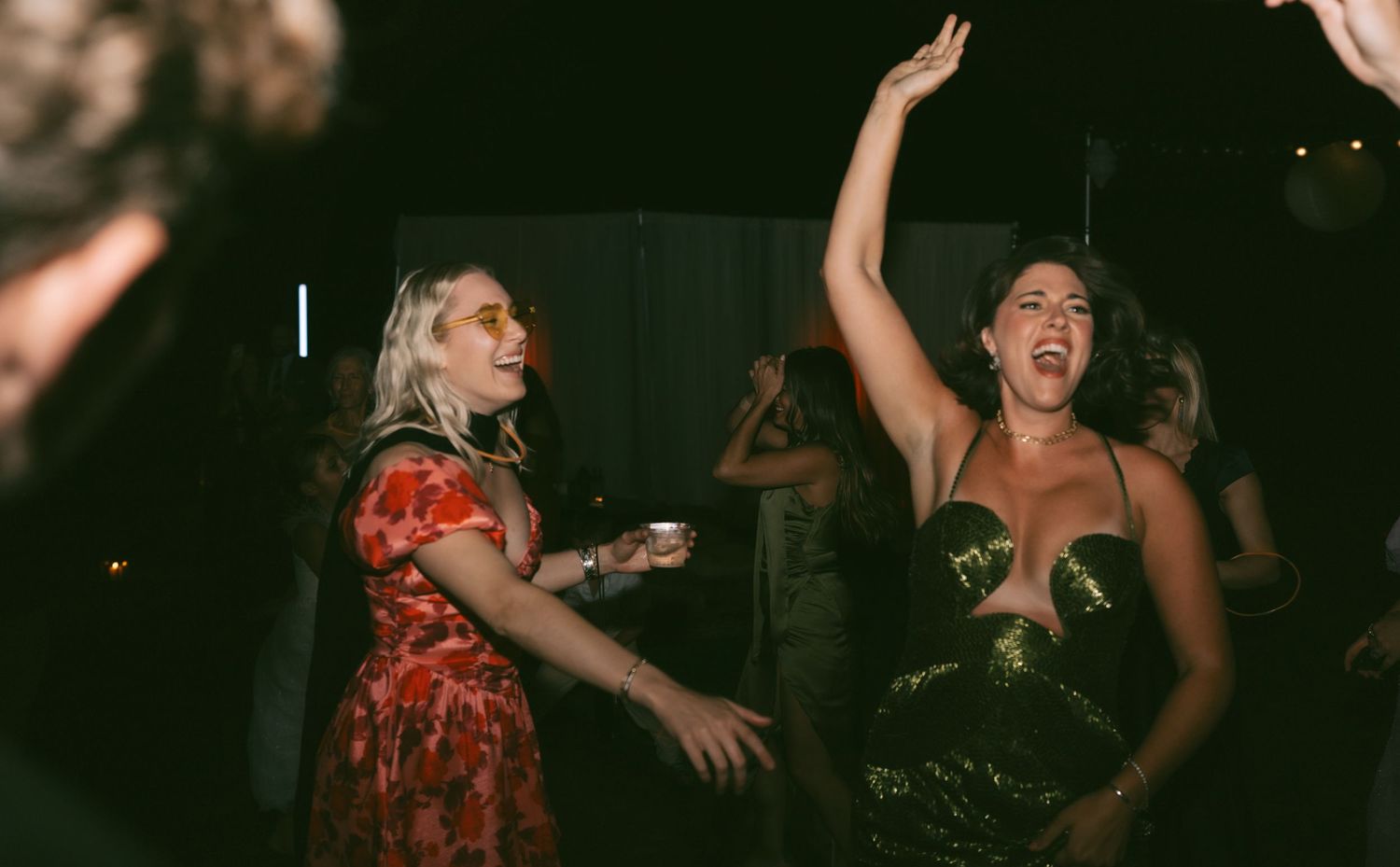 Wedding guests dancing enthusiastically at a dimly lit reception party.