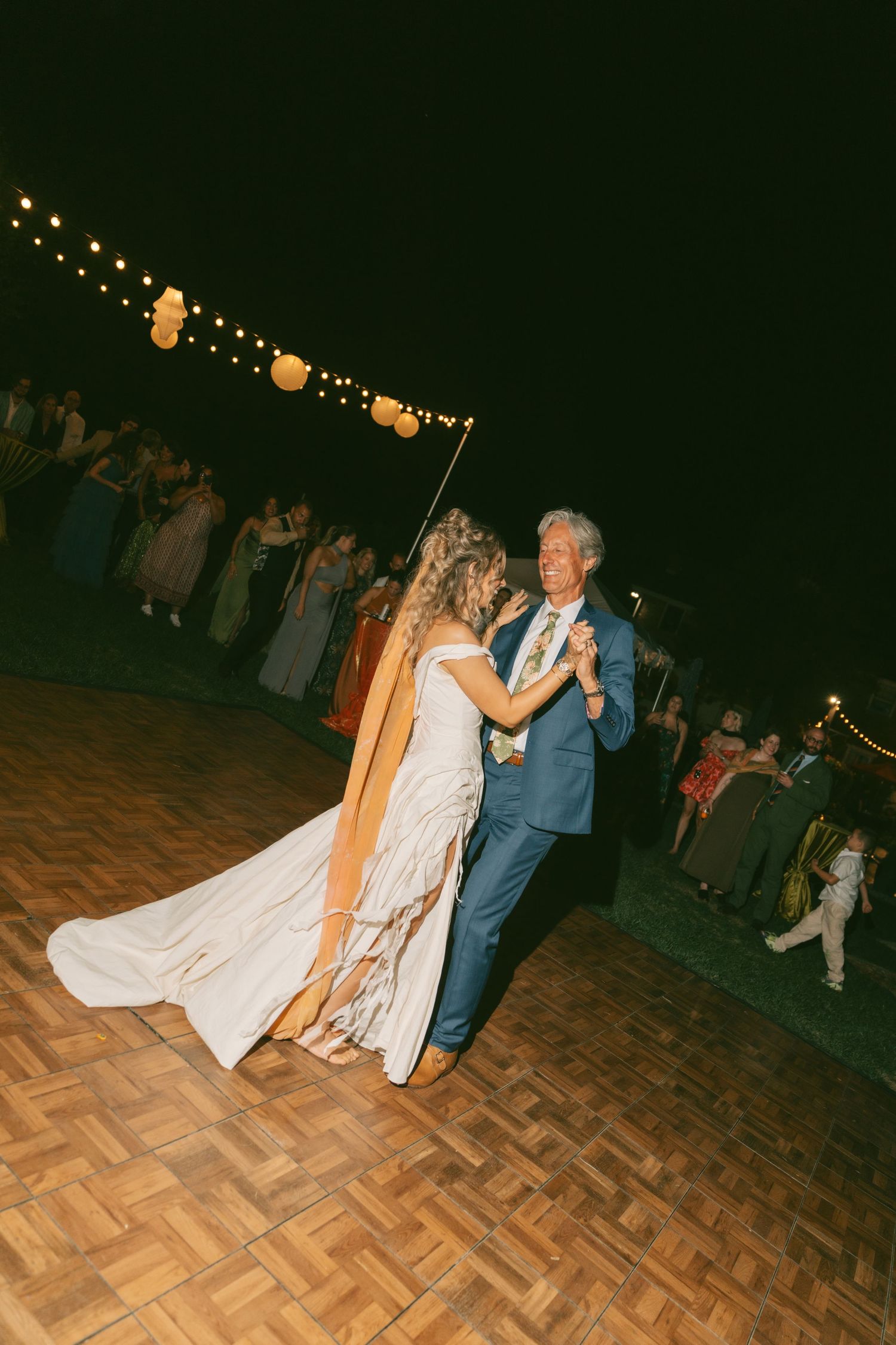 Evening wedding reception dance on a wooden parquet floor under string lights.