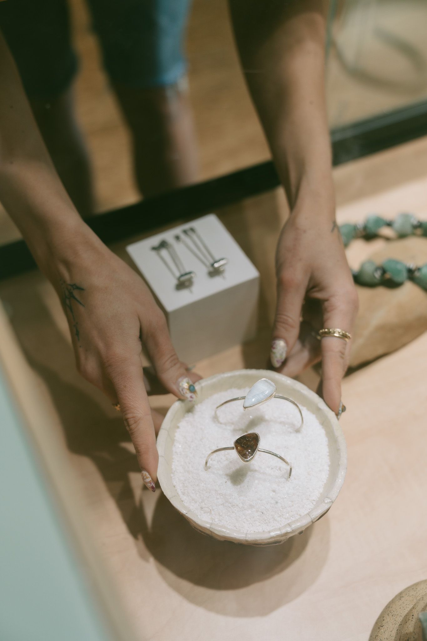 Jewler from Suma Jewlery Co placing wedding rings on white sand in an artistic arrangement.