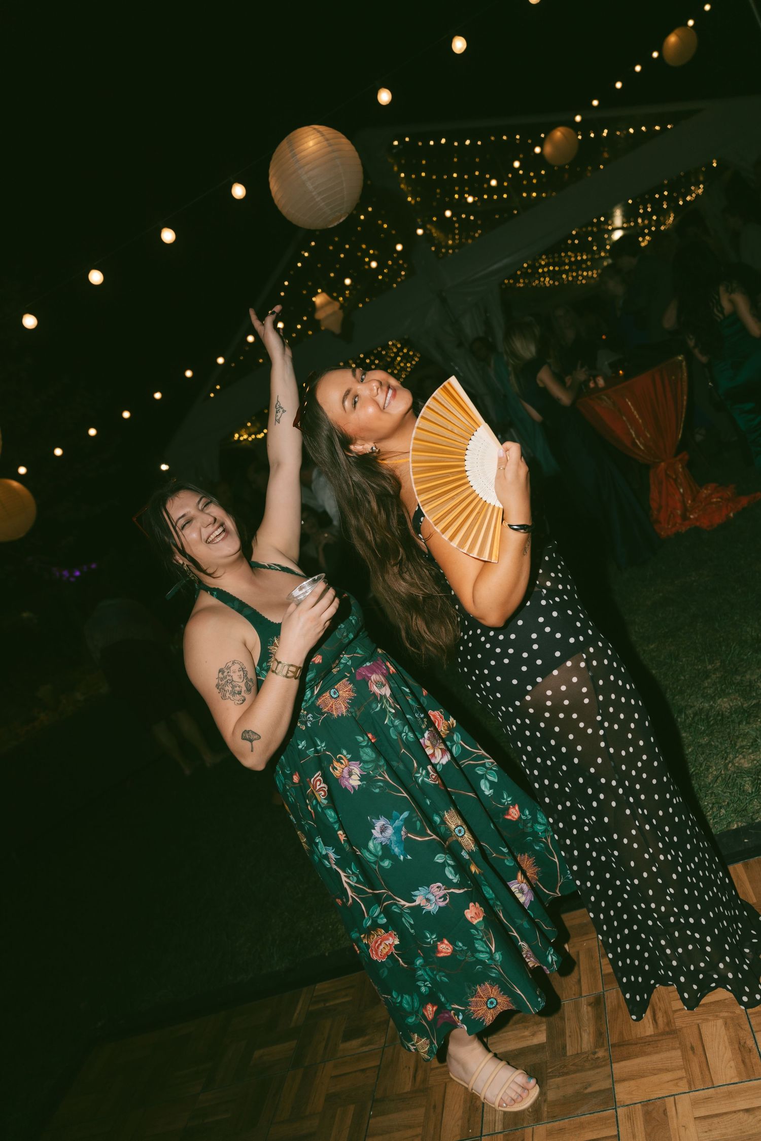 People dancing and having fun on a wooden dance floor under string lights at a nighttime party.