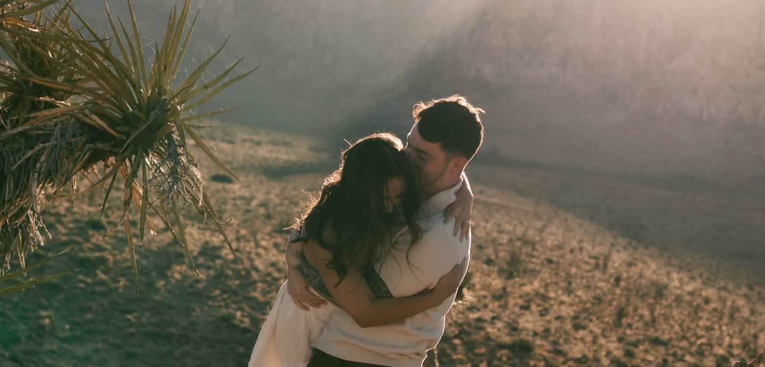 A couple shares a tender embrace while backlit by golden sunlight in a desert landscape in Las Vegas, NV.