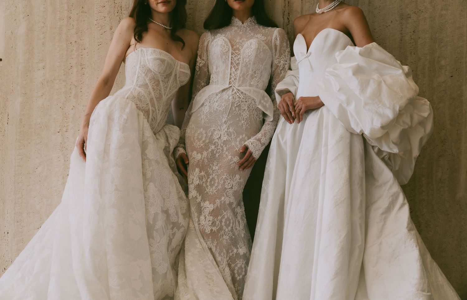 Collection of wedding gowns displayed against textured concrete wall in natural light.
