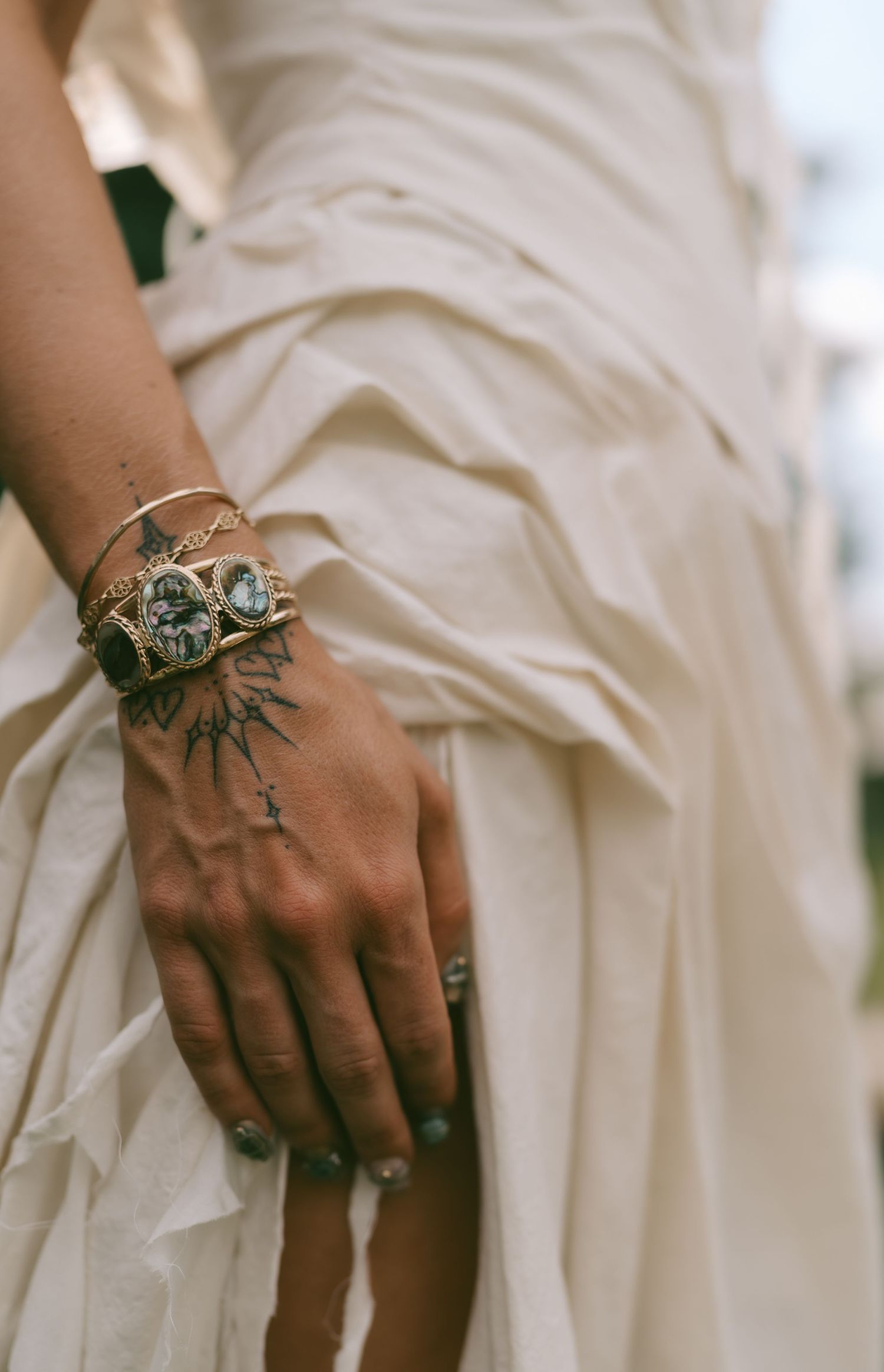 Close-up of ornate rings and jewelry on hands against white fabric.