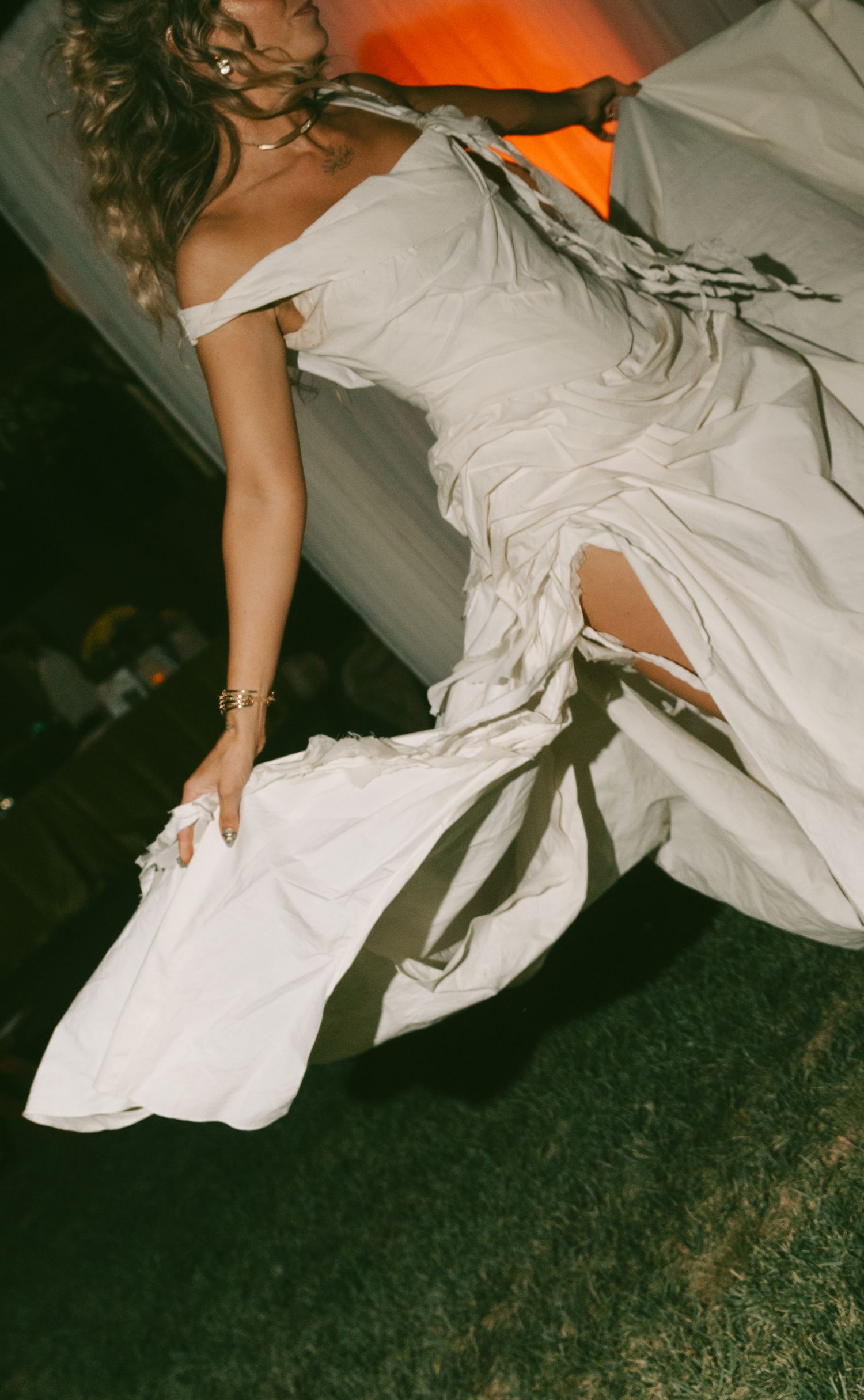 Dramatic fashion photo of white dress flowing across green grass at sunset.