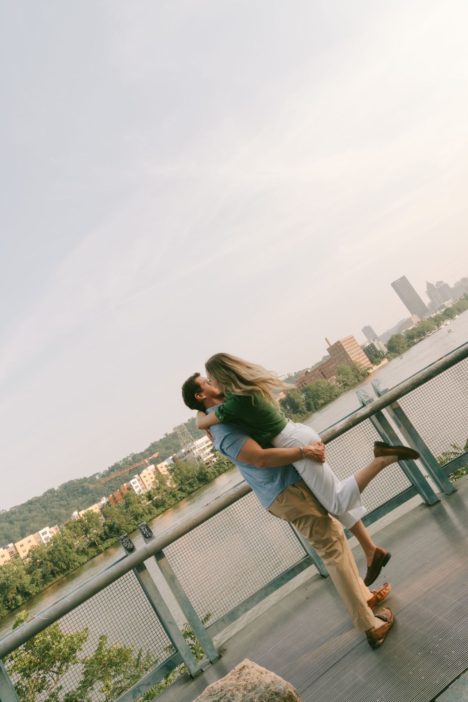 People playfully pose along a riverside railing with a city skyline in the background.