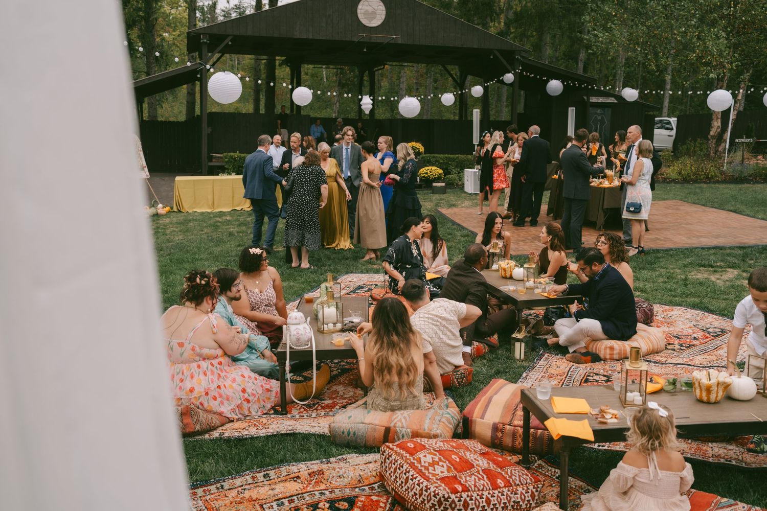 A romantic outdoor wedding reception with string lights and coral tablecloths set among trees at dusk.