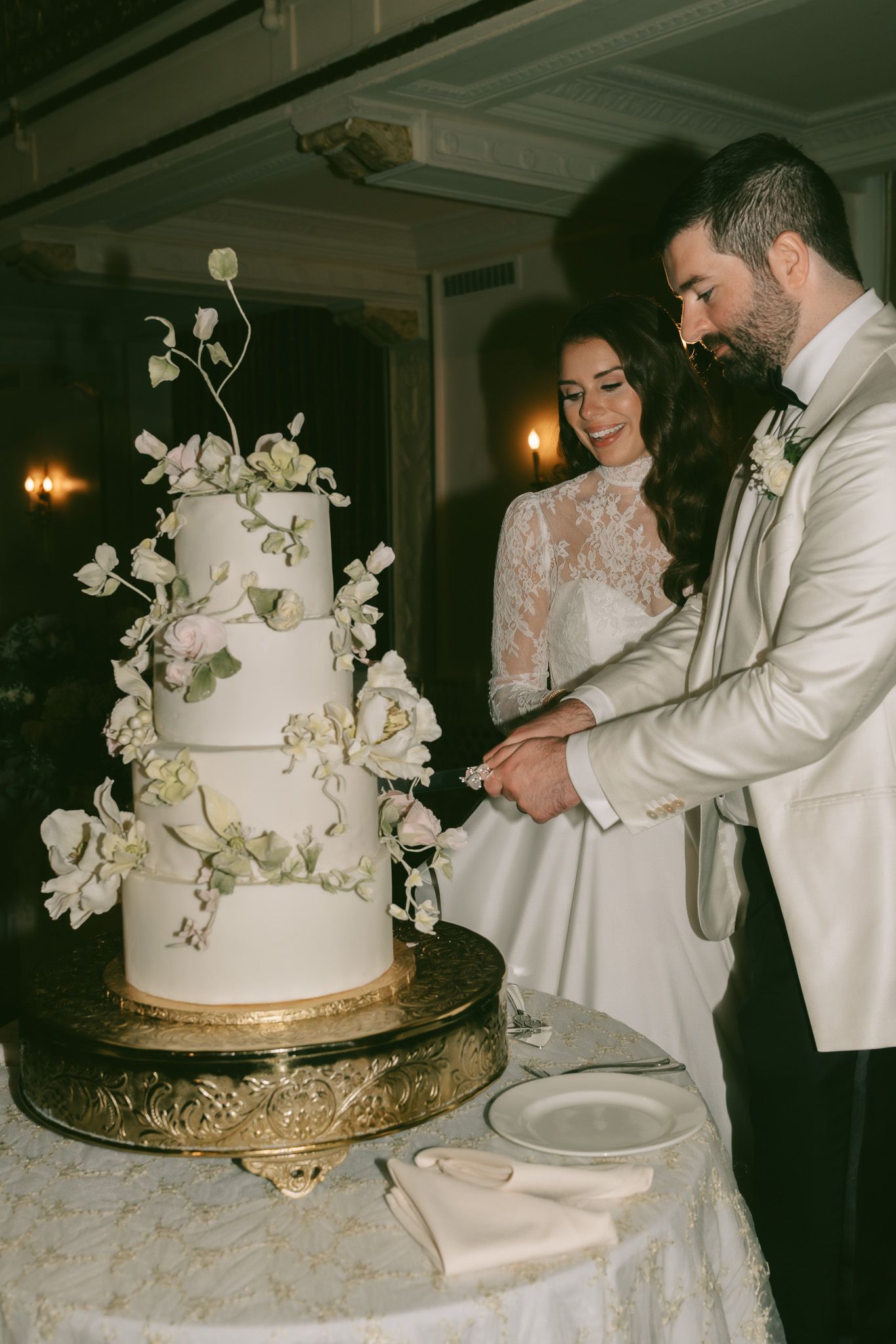Elegant white wedding cake with cascading floral decorations being cut by newlyweds in downtown pittsburgh, pa.