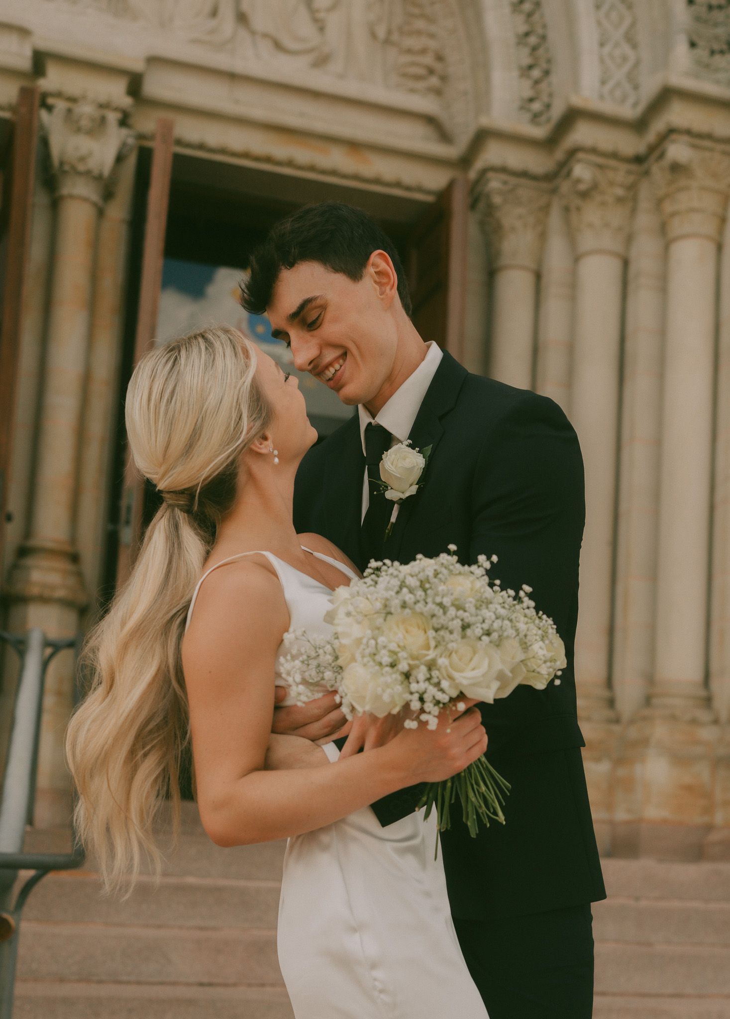 Romantic wedding sequence showing couple dancing with white flowers against ornate architecture.