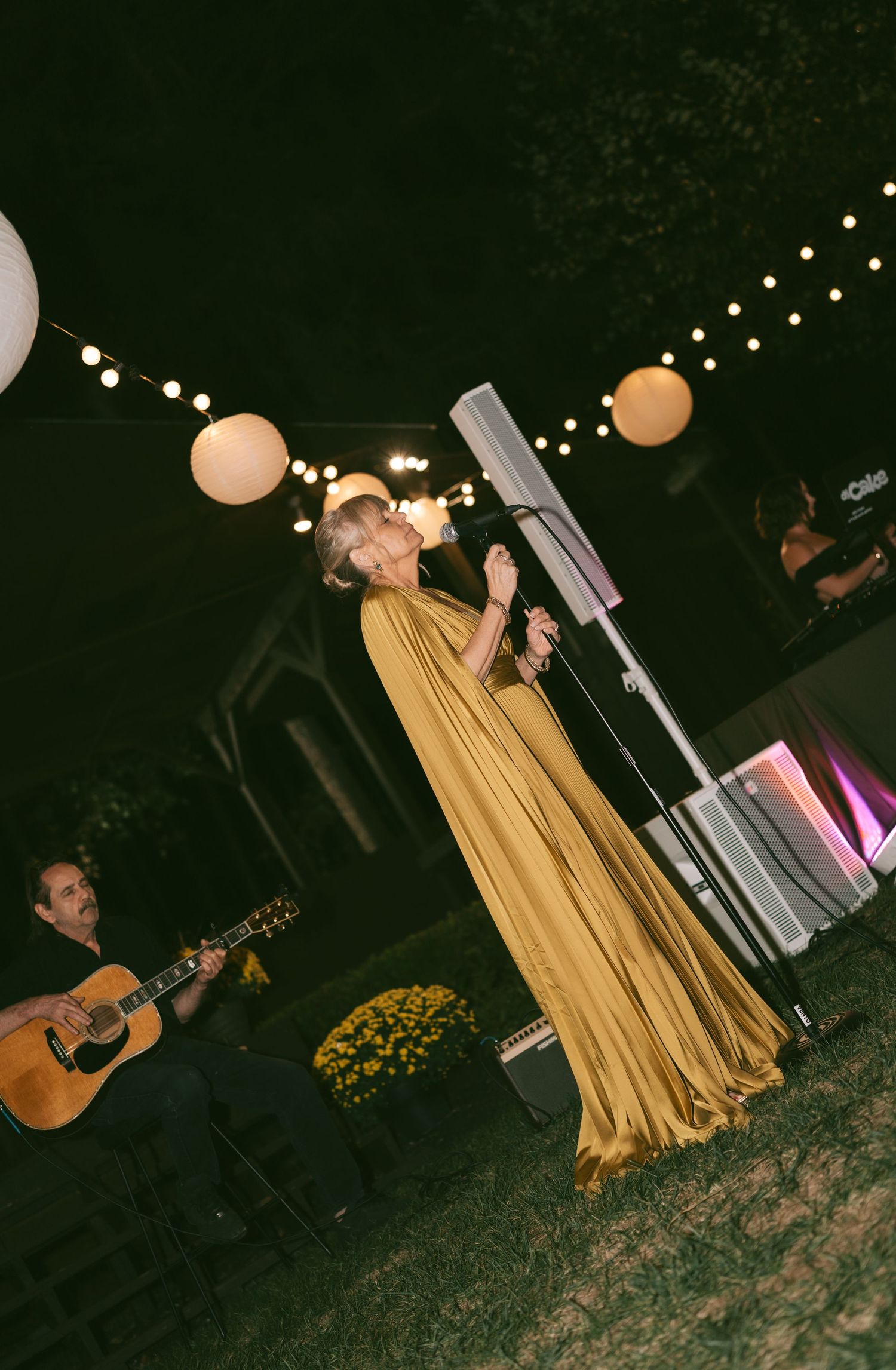 Evening outdoor reception with string lights and musicians performing under dark sky.