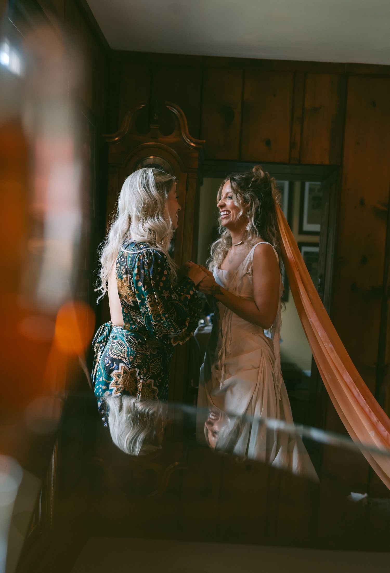 Wedding preparation scene with dress adjustments reflected in vintage mirrors.