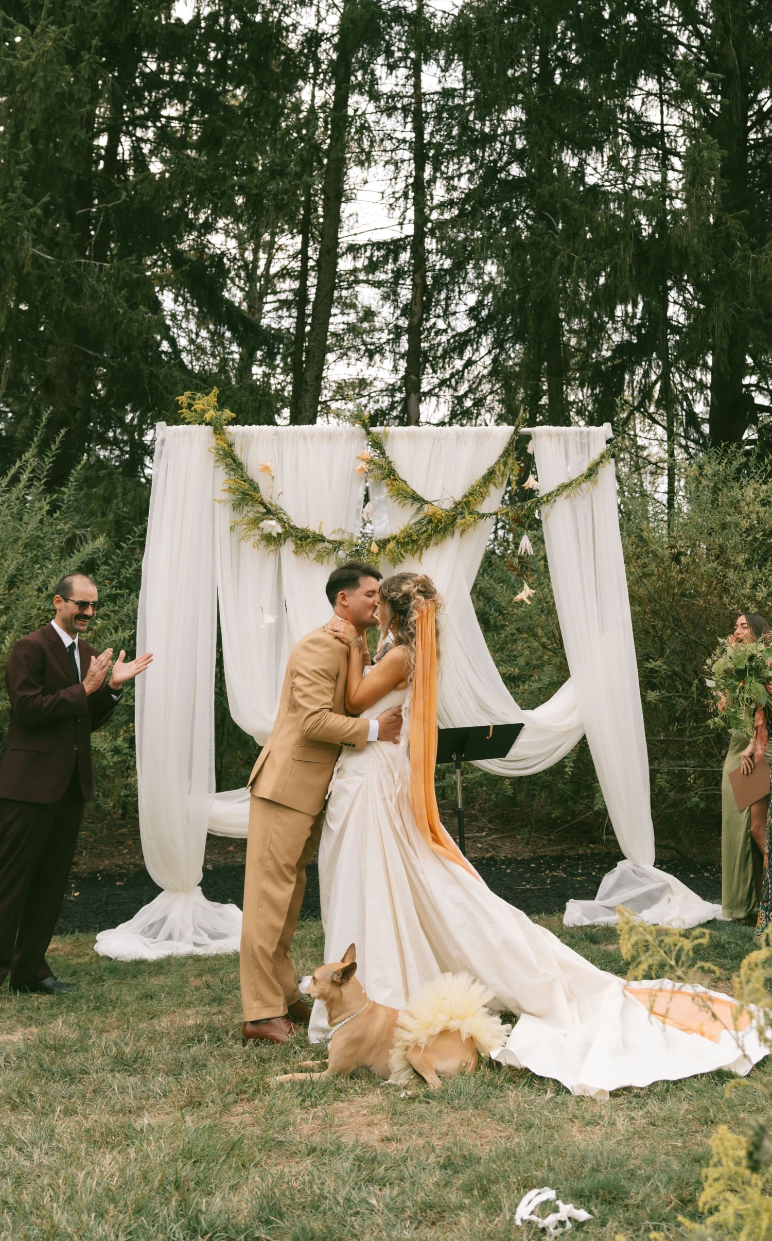Outdoor wedding ceremony setup with white draped fabric and greenery garland in a wooded setting.
