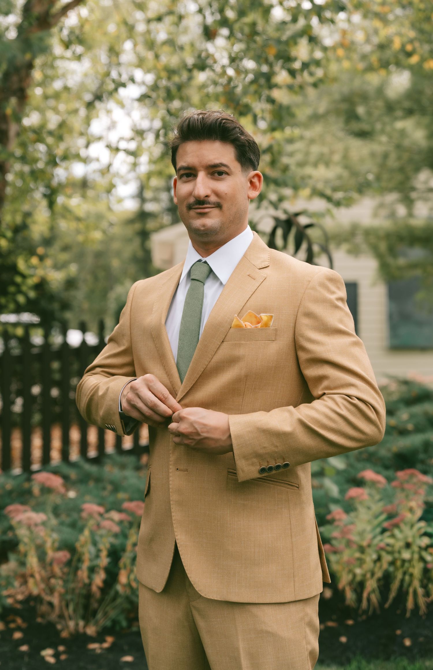 A series of photos showing a person in a tan suit with a blue tie posing outdoors in a garden setting.