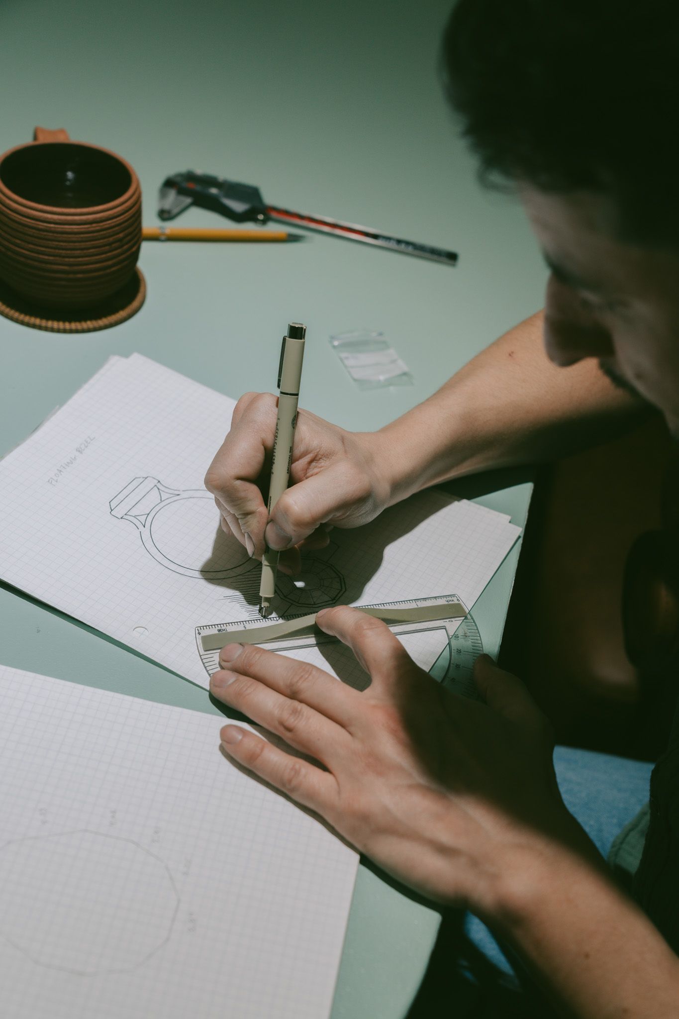 Jewler from Suma Jewlery Co sketching or drawing on graph paper with art supplies visible.