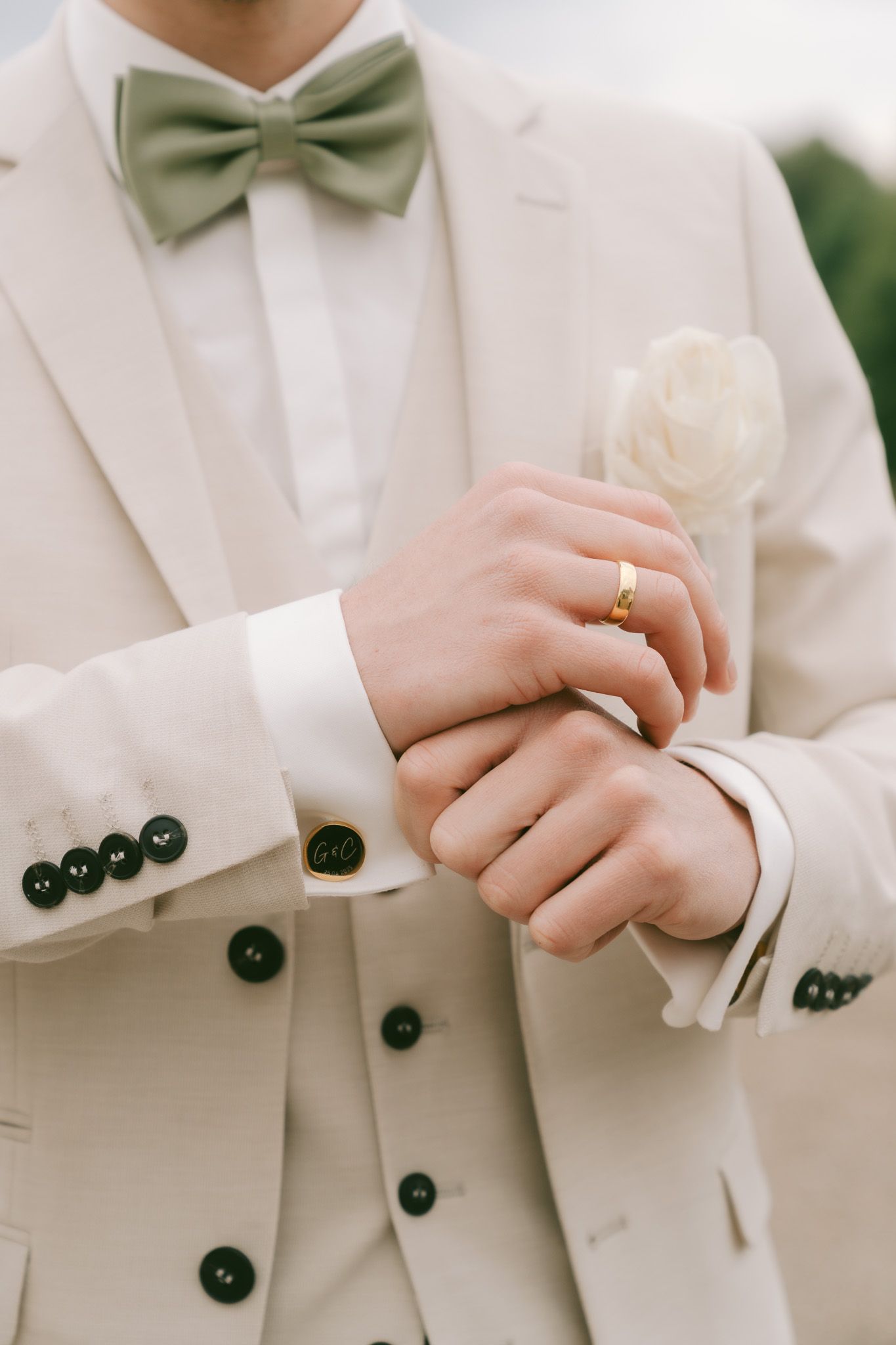 Close-up of groom's cream suit with sage bow tie and white rose boutonniere in Germany.
