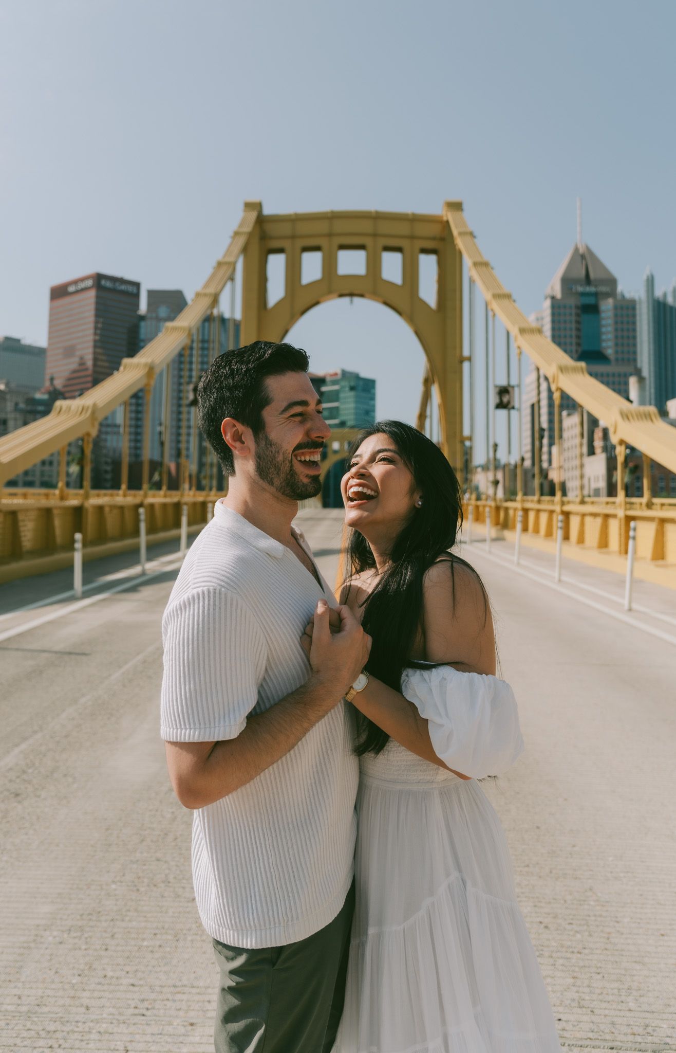 A couple sharing a joyful moment together on Pittsburgh's iconic yellow Roberto Clemente Bridge with the city skyline behind them in north.