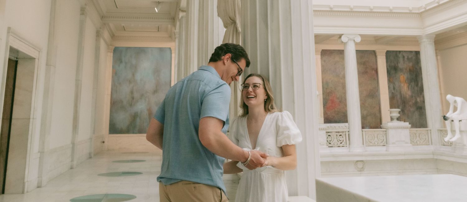 Couple walking through a minimalist art gallery with white walls and skylights.