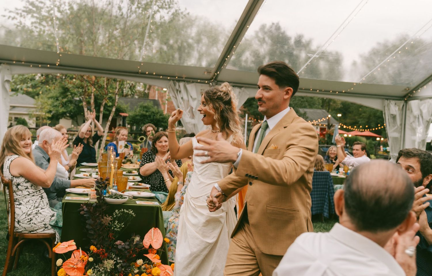 Wedding guests celebrate under a white tent during an outdoor reception on a misty day.