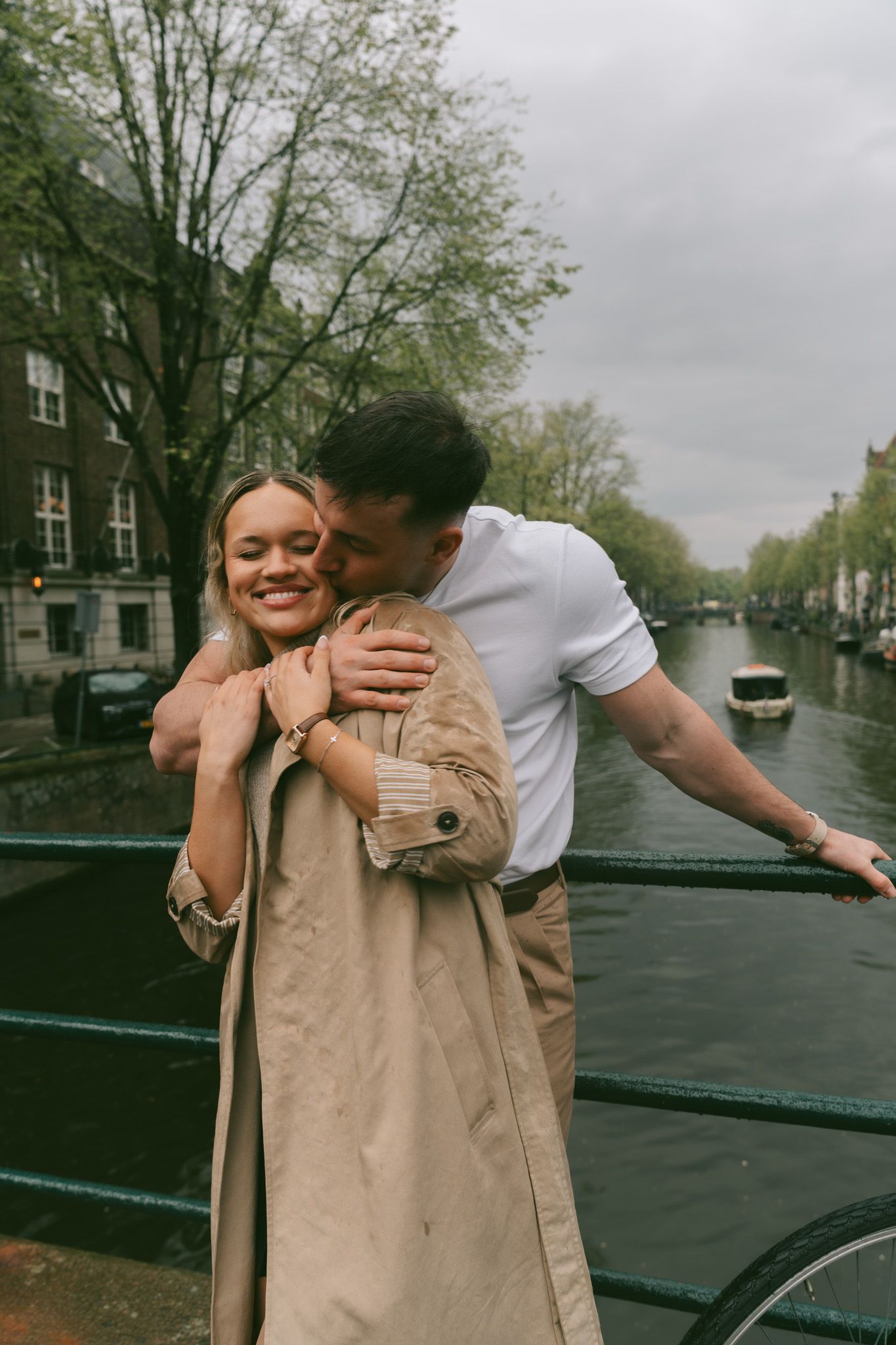Affectionate scene on an Amsterdam canal bridge with traditional houses in the background.