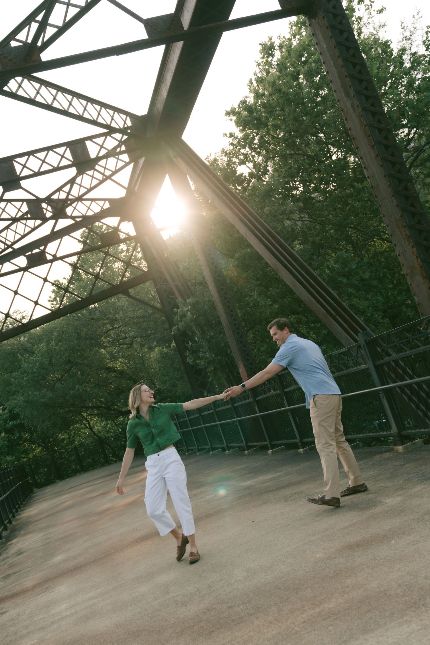 A couple dancing on a bridge at sunset with metal trusses creating dramatic silhouettes.