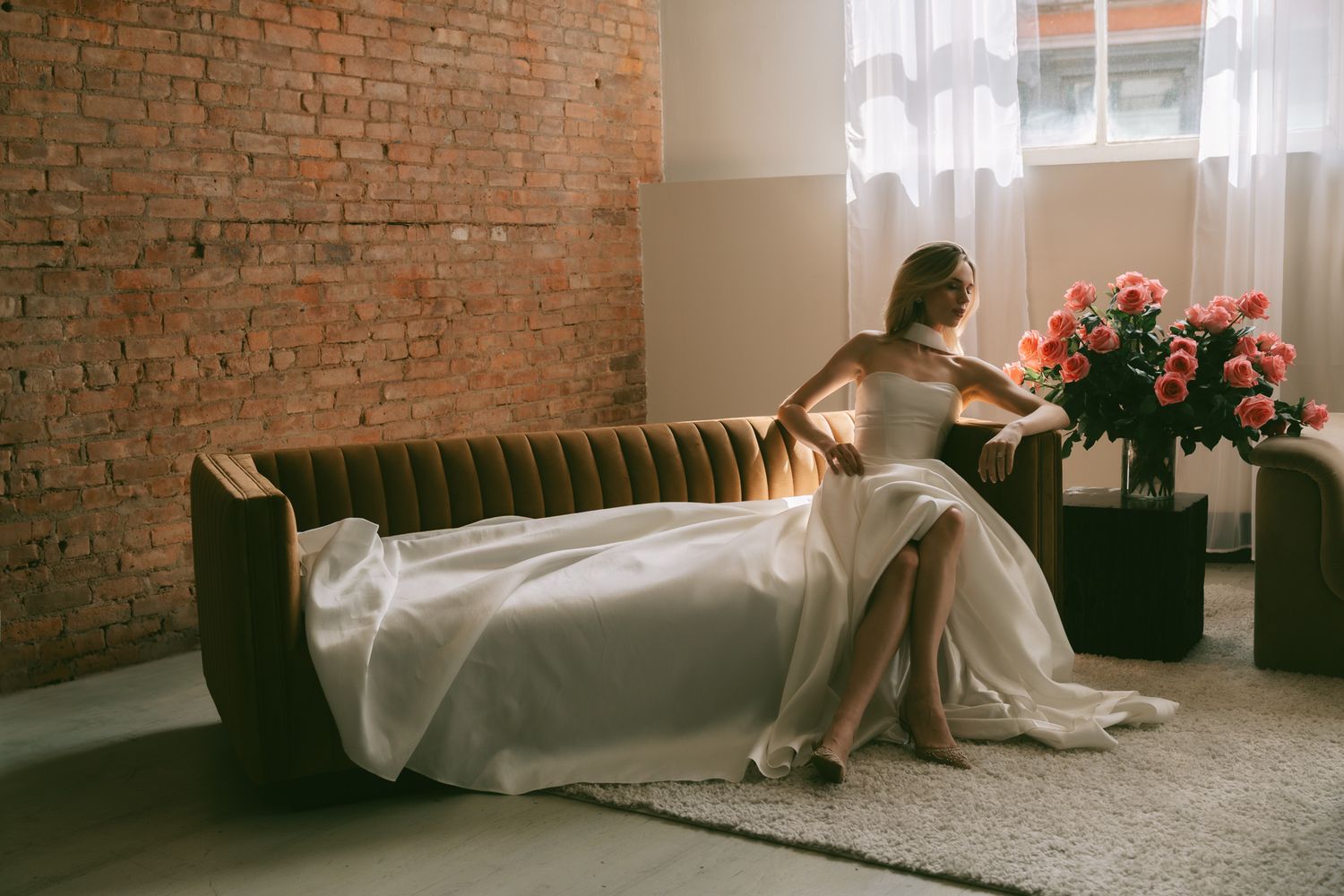 Elegant bridal portrait on a leather couch with flowing white dress and pink roses.