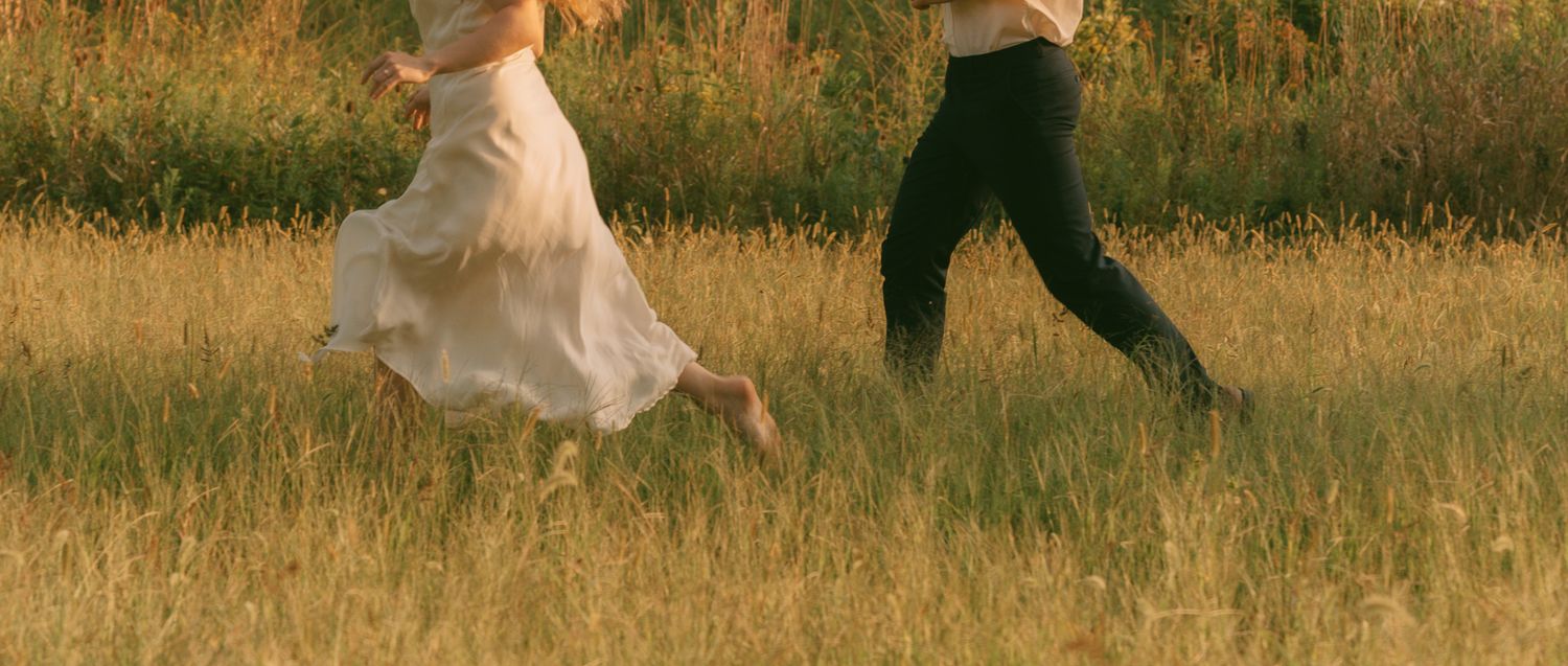 Couple running through a golden wheat field at sunset.