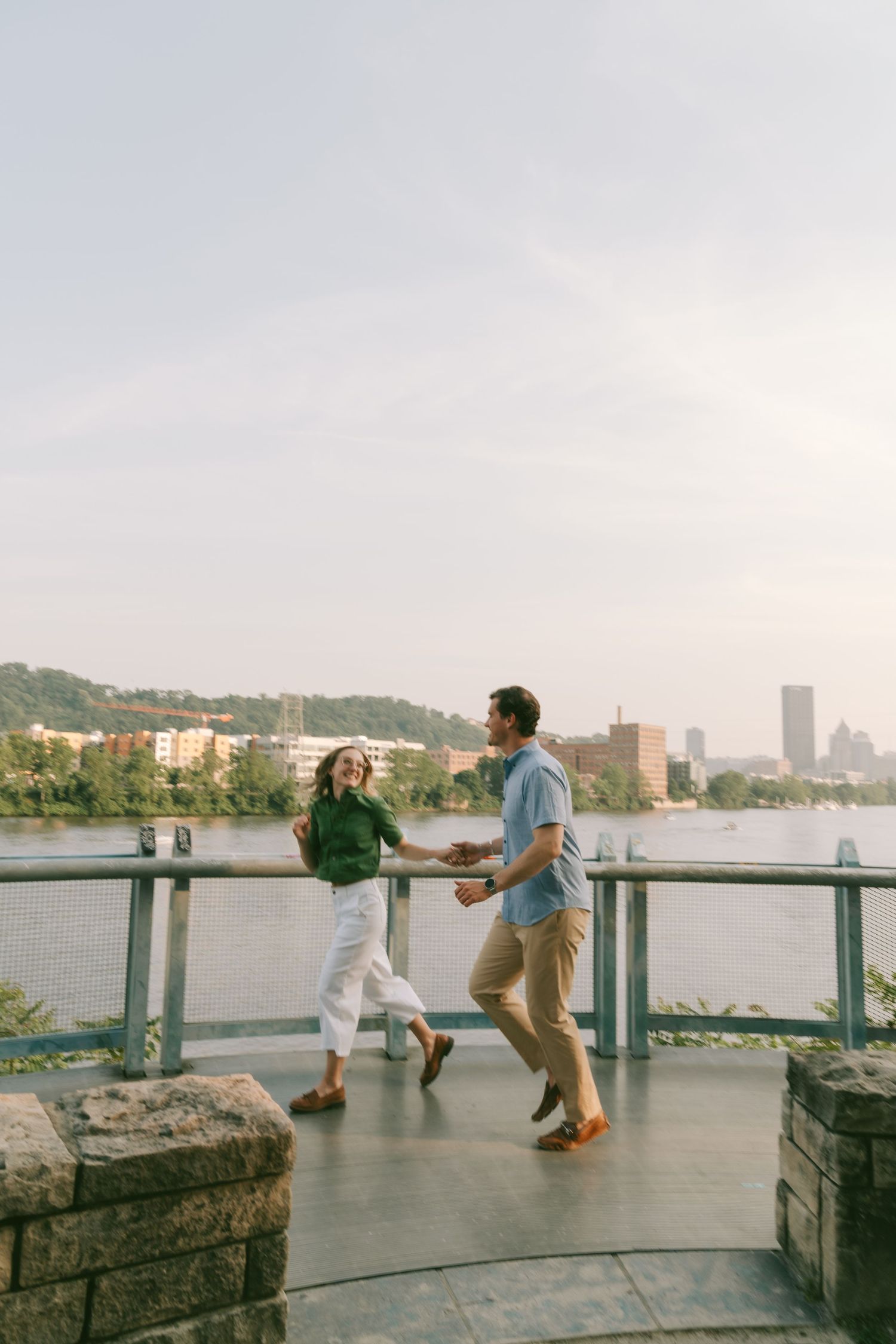 Scenic waterfront overlook with stone railing against a cityscape backdrop during golden hour.