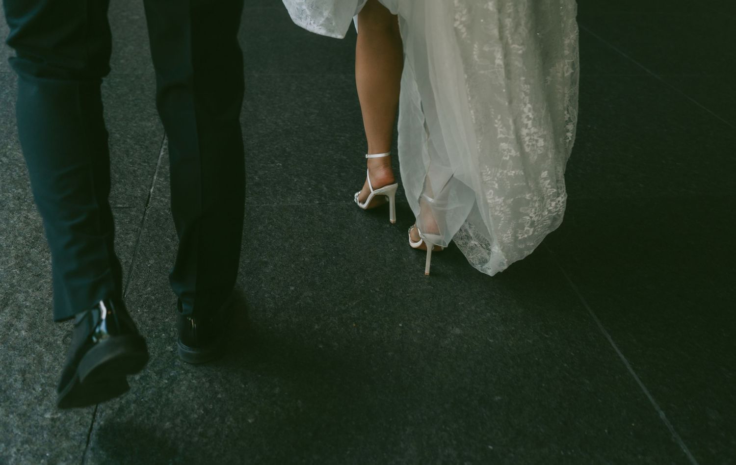 A wedding couple's feet dance together on a dark hardwood floor during their first dance.