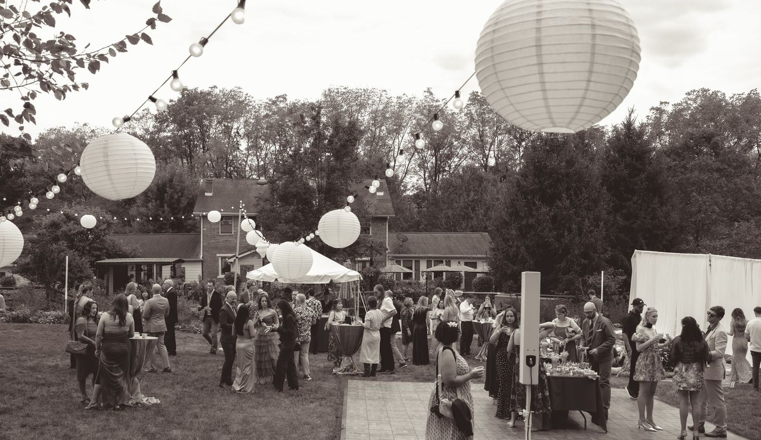 White paper lanterns and guests gathered at an outdoor wedding reception under evening sky.