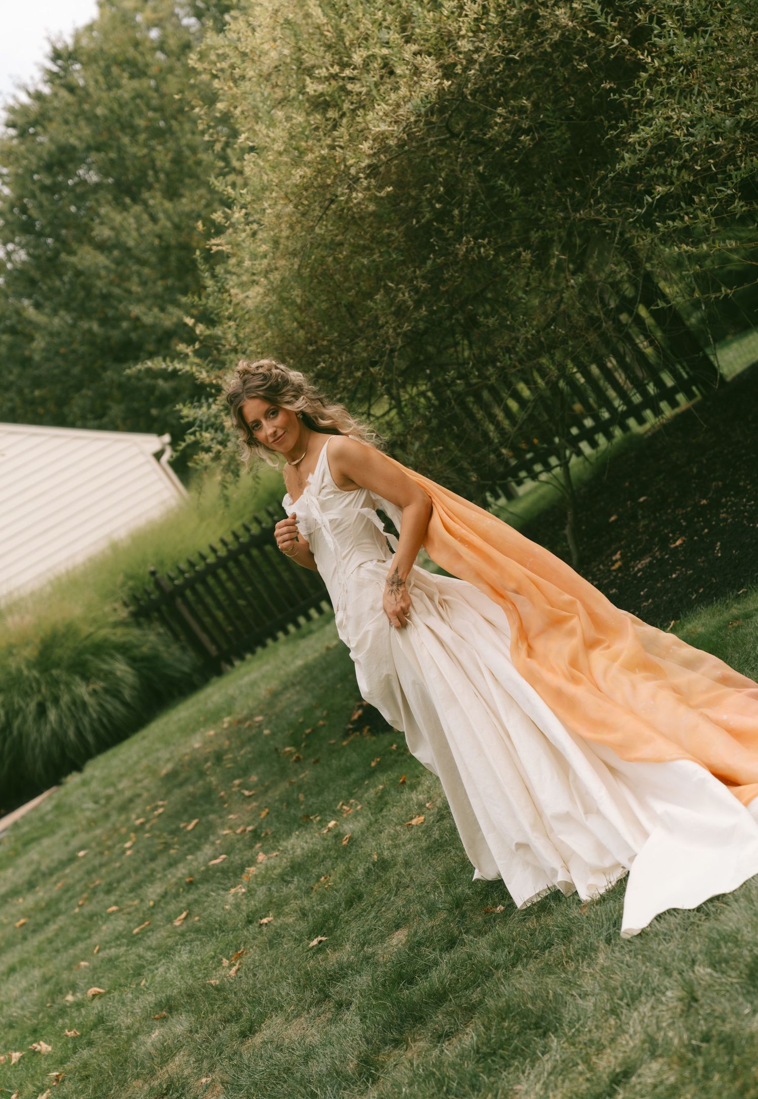 White wedding dress flowing in the breeze on a grassy hillside during golden hour.