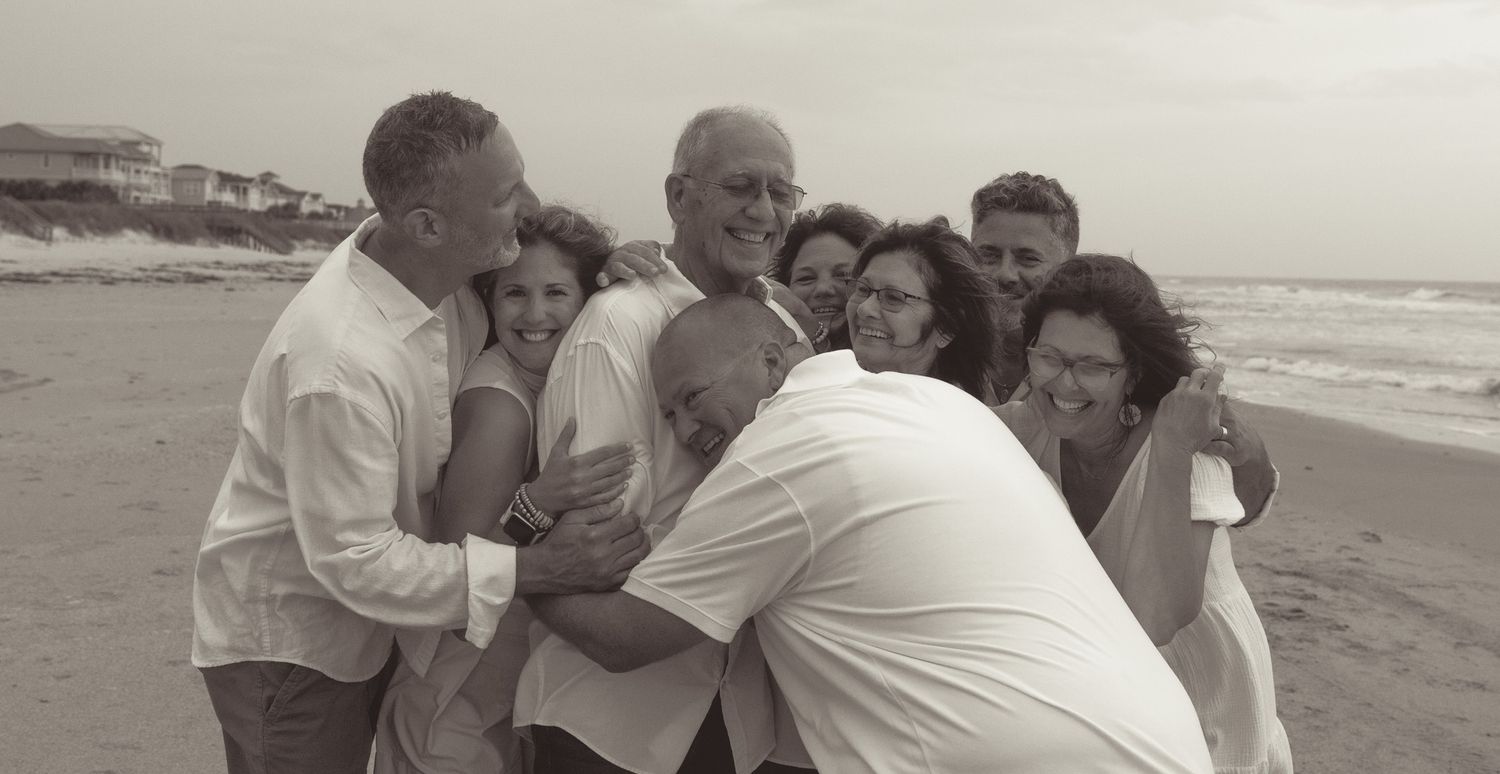 Group of people hugging closely together while enjoying a moment on a beach in black and white.