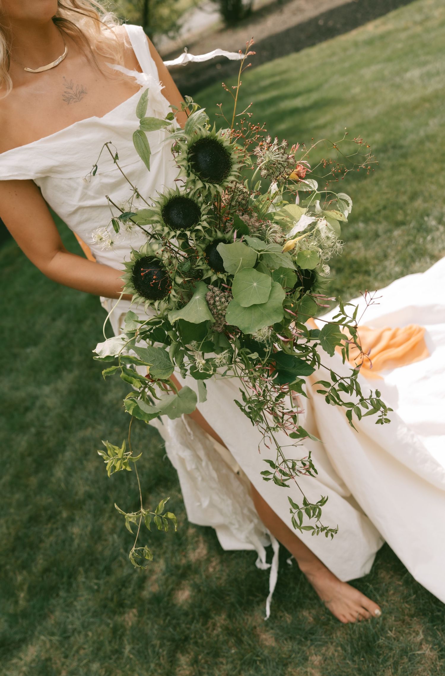 Elegant wedding bouquet featuring wild greenery and white flowers against a flowing white dress.