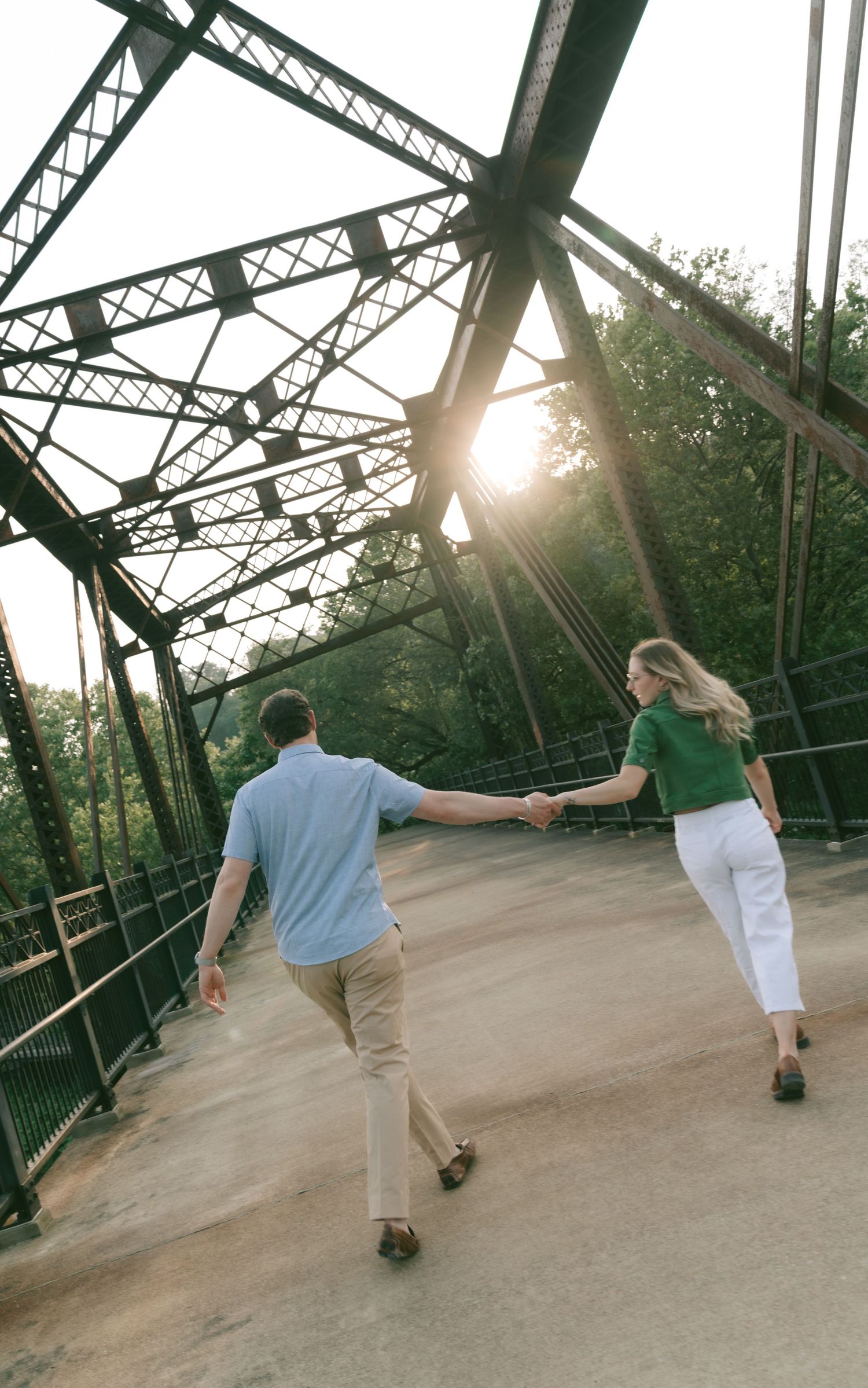 Couple holding hands while walking across a steel bridge at sunset.