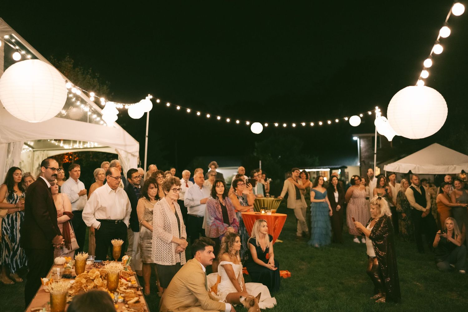 Outdoor wedding reception at night with string lights and paper lanterns creating ambient atmosphere.
