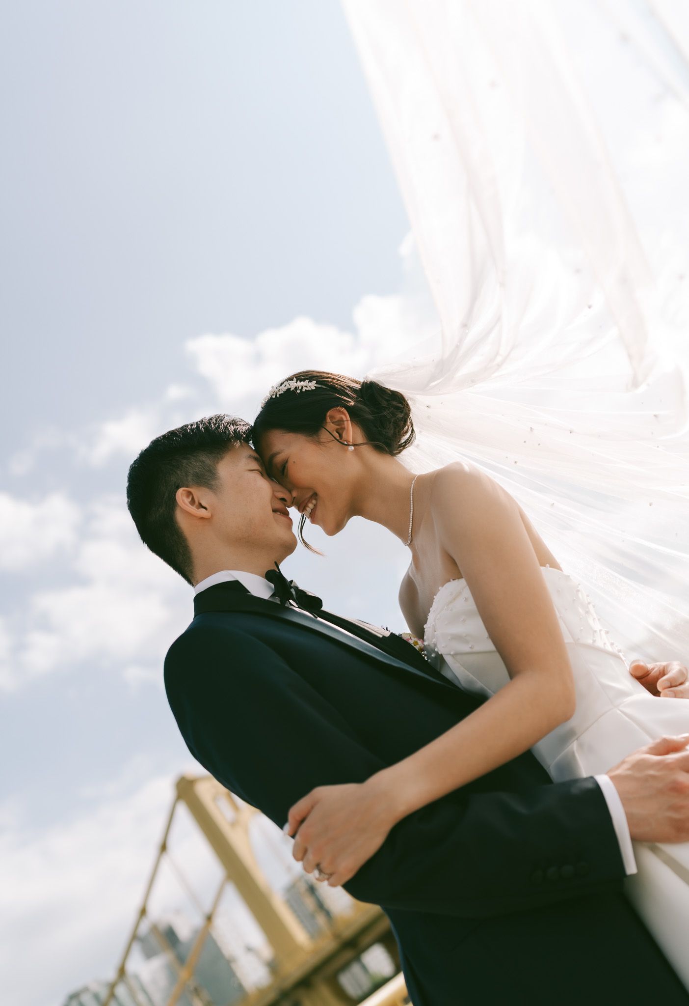 Romantic wedding couple sharing an intimate moment under flowing veil against blue sky infront of the yellow bridges in downtown Pittsburgh.