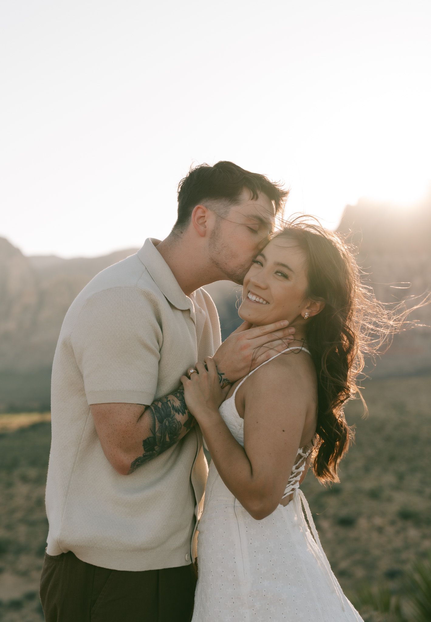 A tender romantic moment between a couple in beige and white attire against a sunlit outdoor backdrop at golden hour in red rock canyon, NV