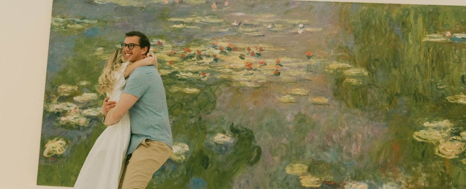 A couple embraces in front of a large Monet water lilies painting display.