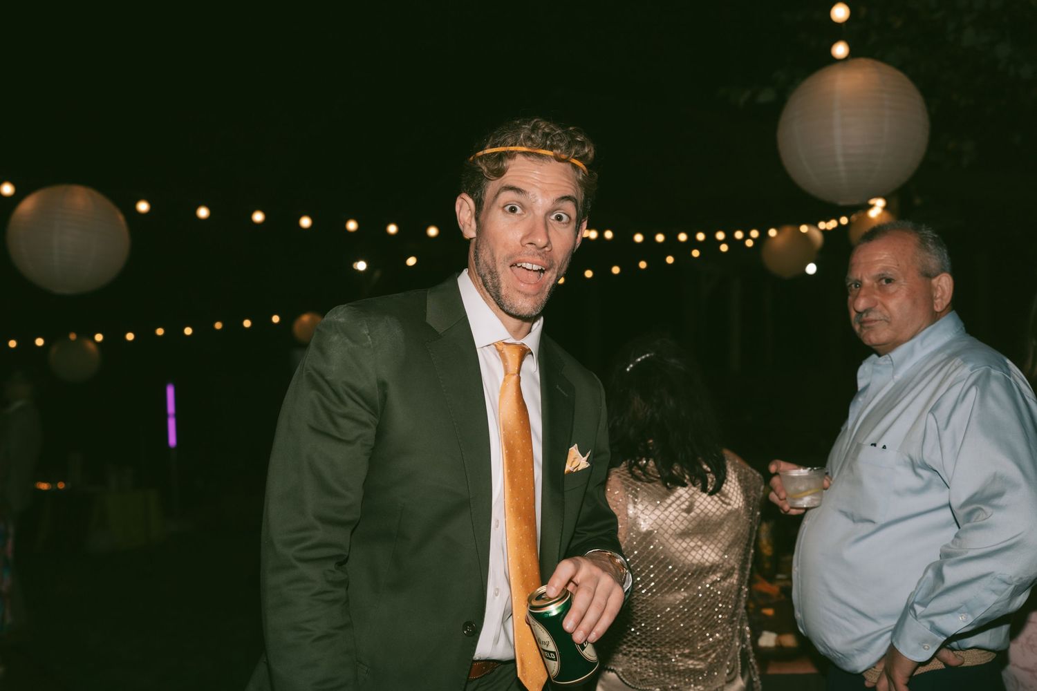 Evening wedding reception with guests dancing under string lights and glowing lanterns.