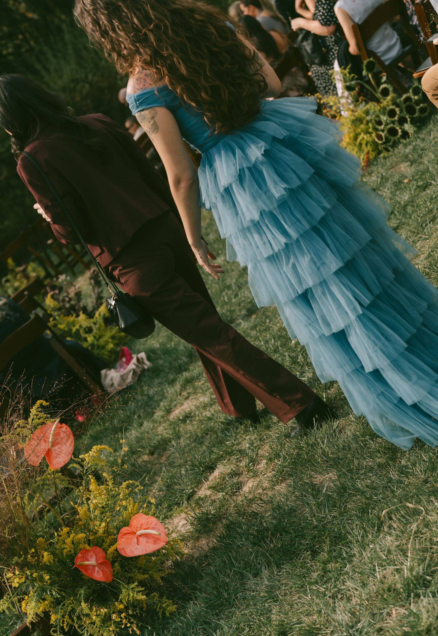 A flowing blue tiered tulle dress photographed against garden flowers at an outdoor event.