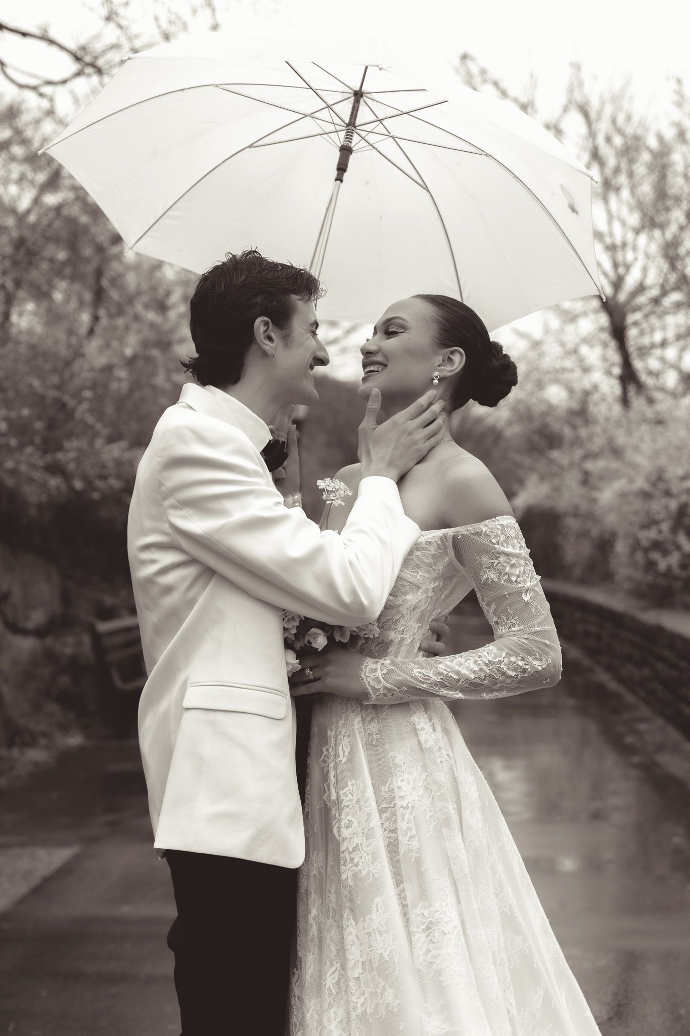 Elegant couple sharing tender moment under white umbrella in black and white photo.