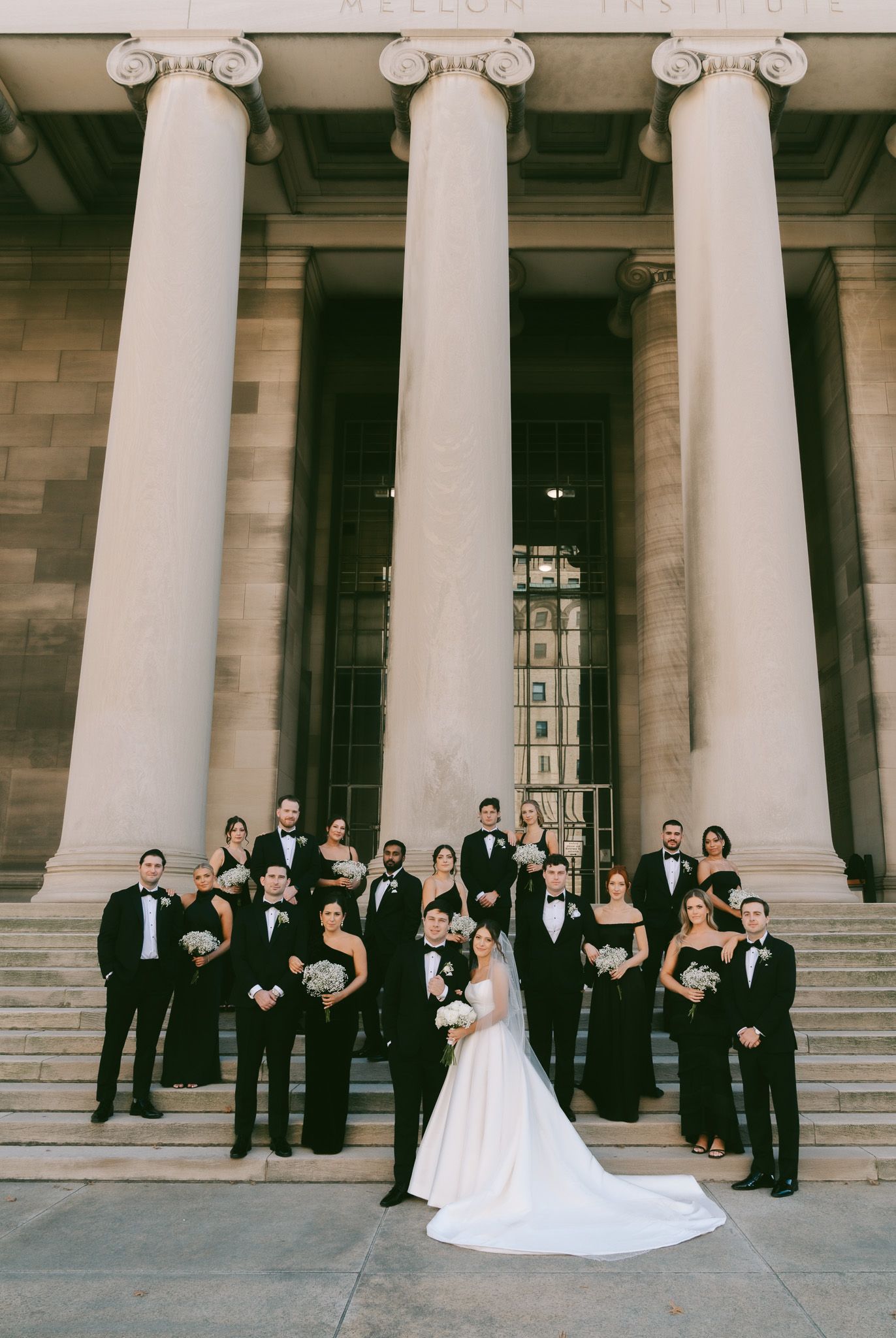 Wedding party poses in front of grand white columns of a classical building in formal attire.
