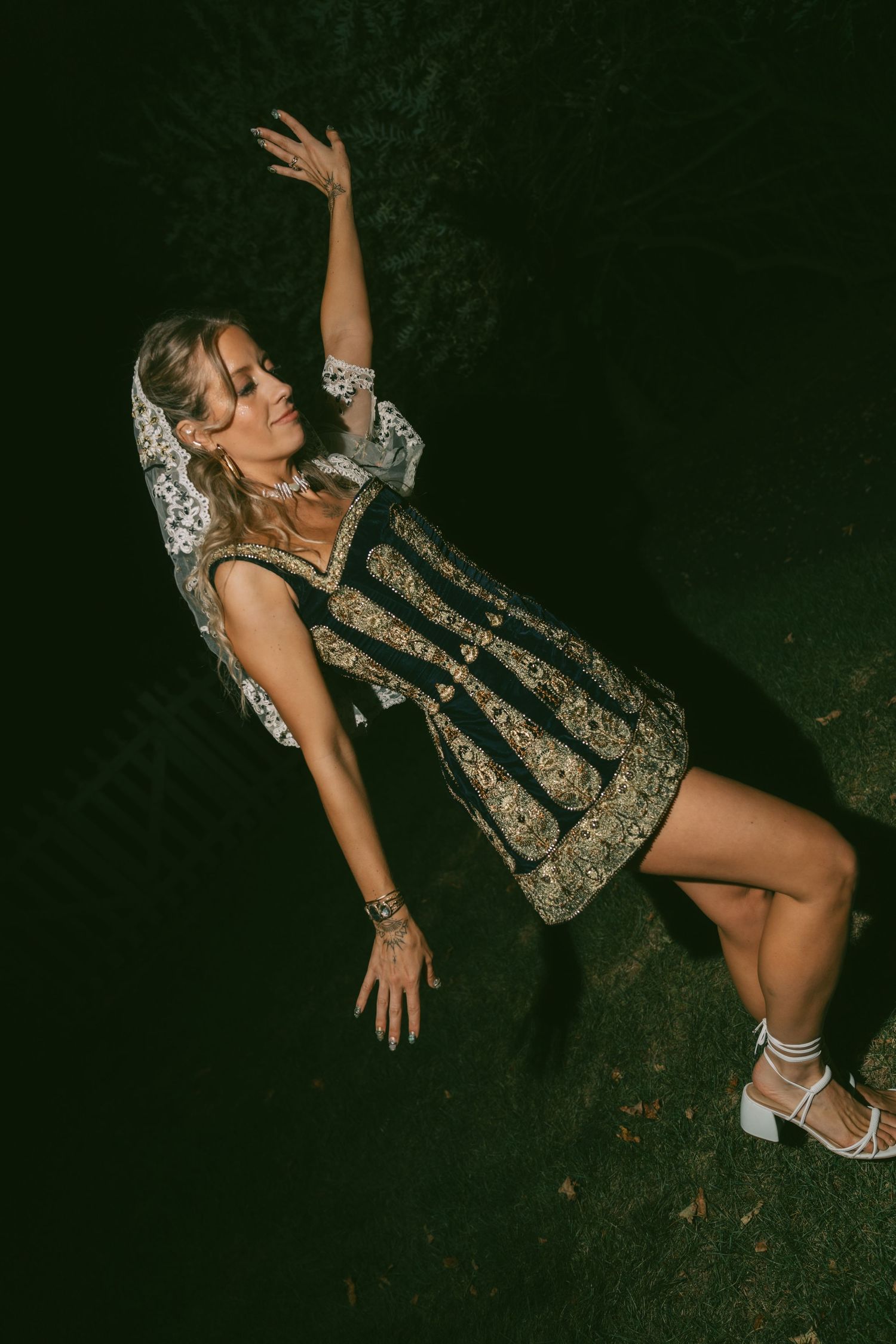 Person in patterned dress dancing and posing dramatically on dark background.