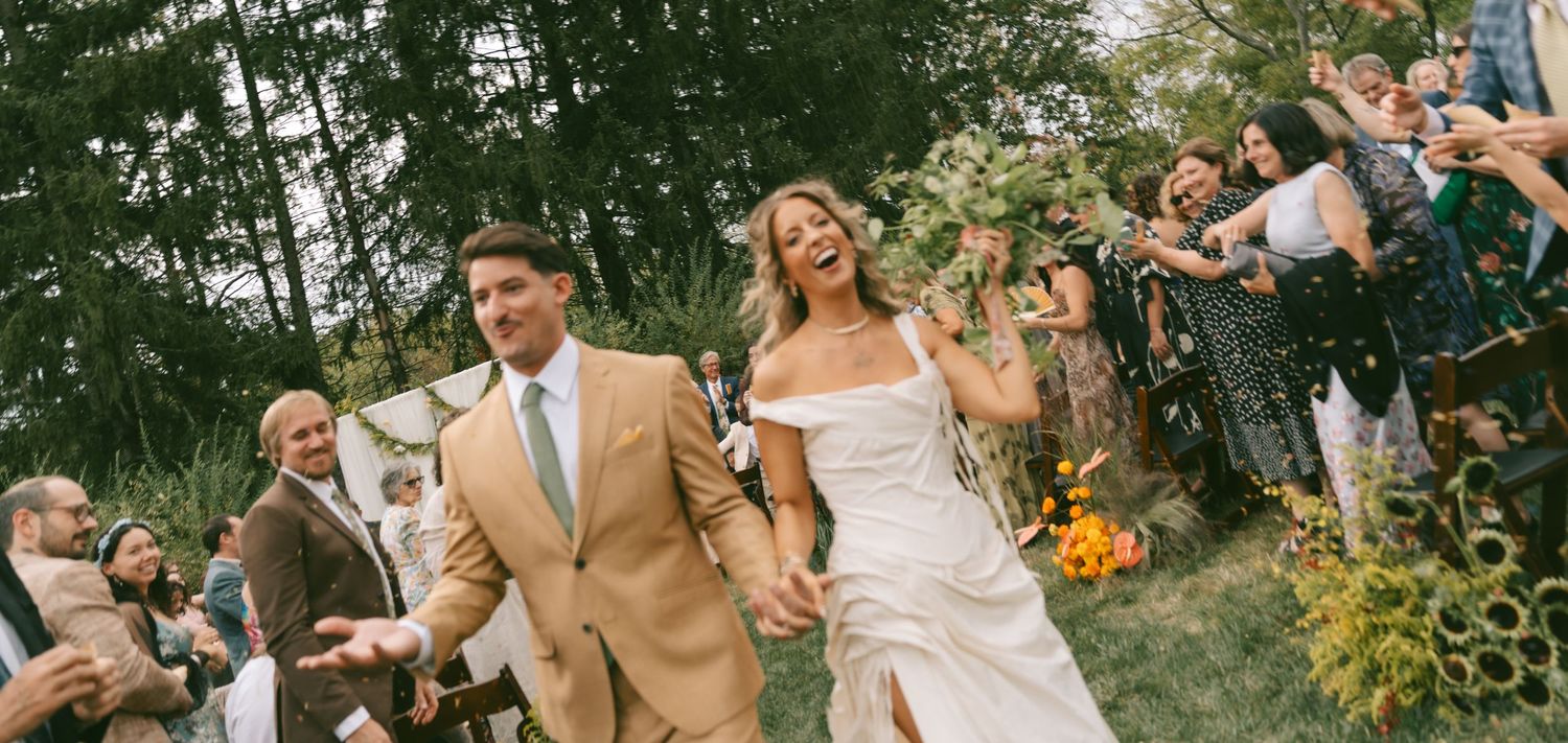 Wedding guests laugh and celebrate together during an outdoor garden ceremony in natural lighting.