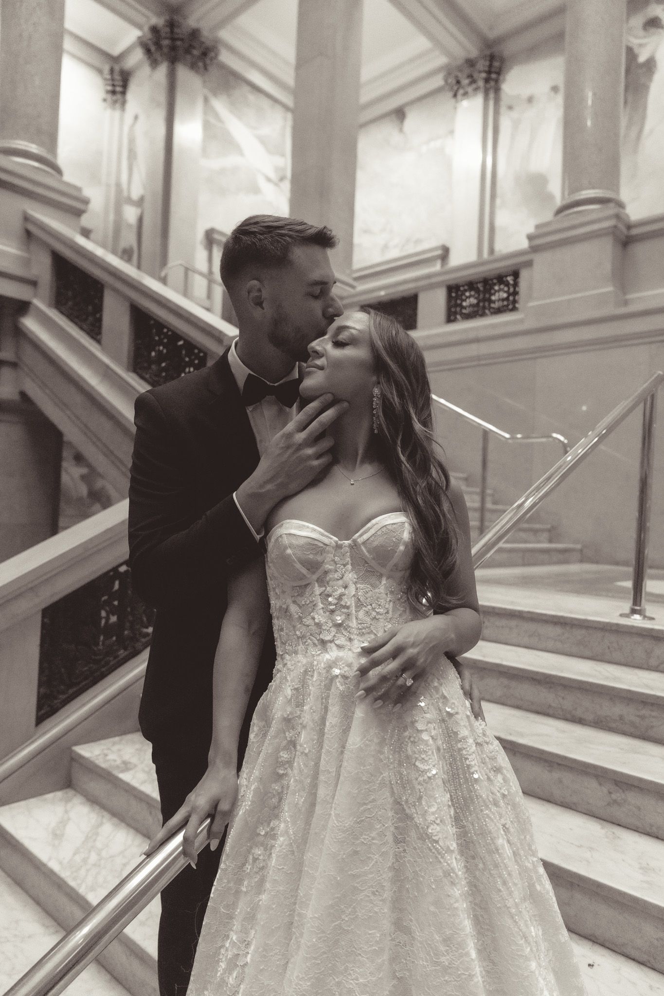 A romantic wedding couple shares intimate moments on an elegant staircase in black and white photography.
