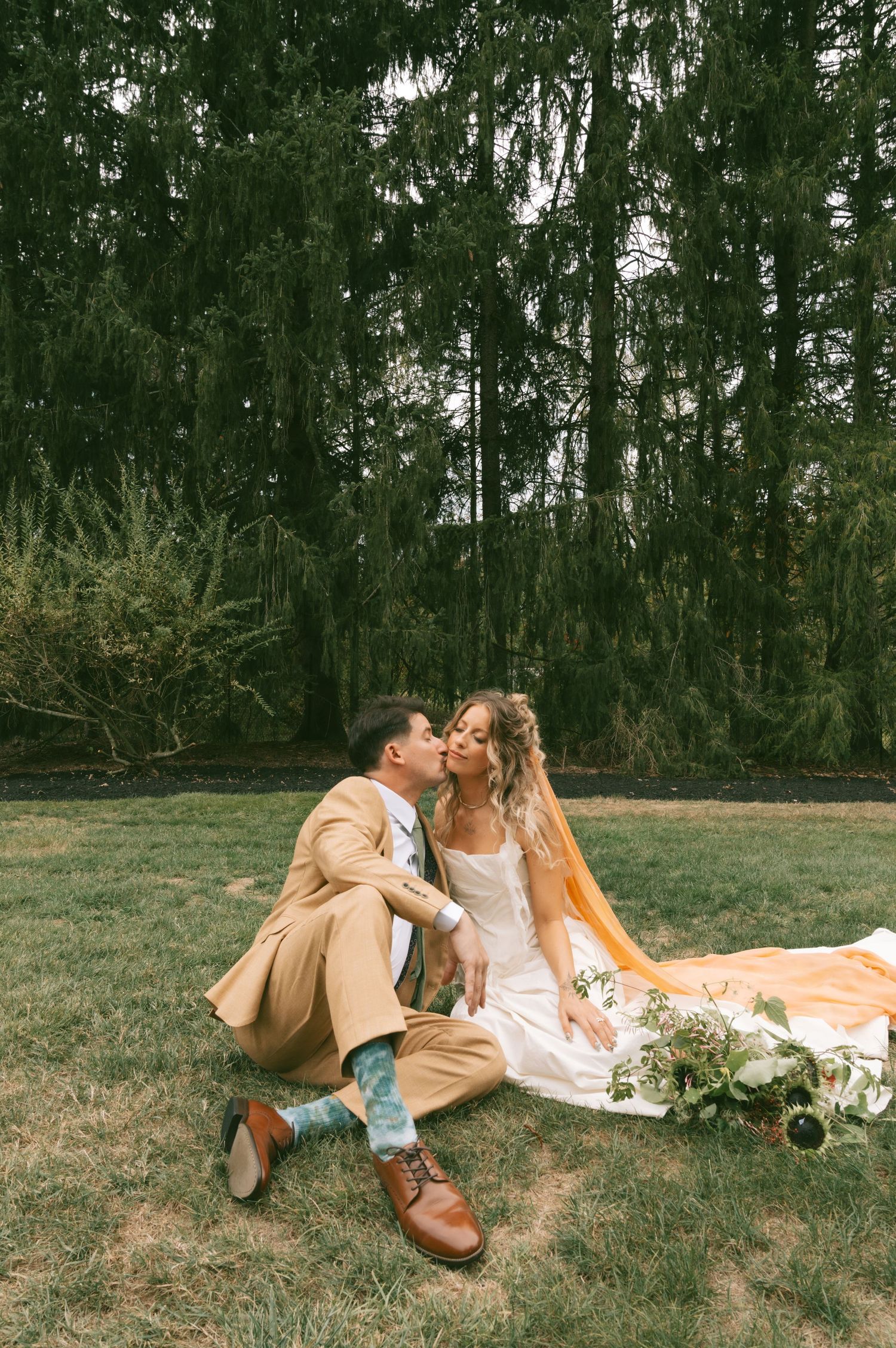 Couple having a romantic picnic on grass with wine and flowers in an outdoor setting.