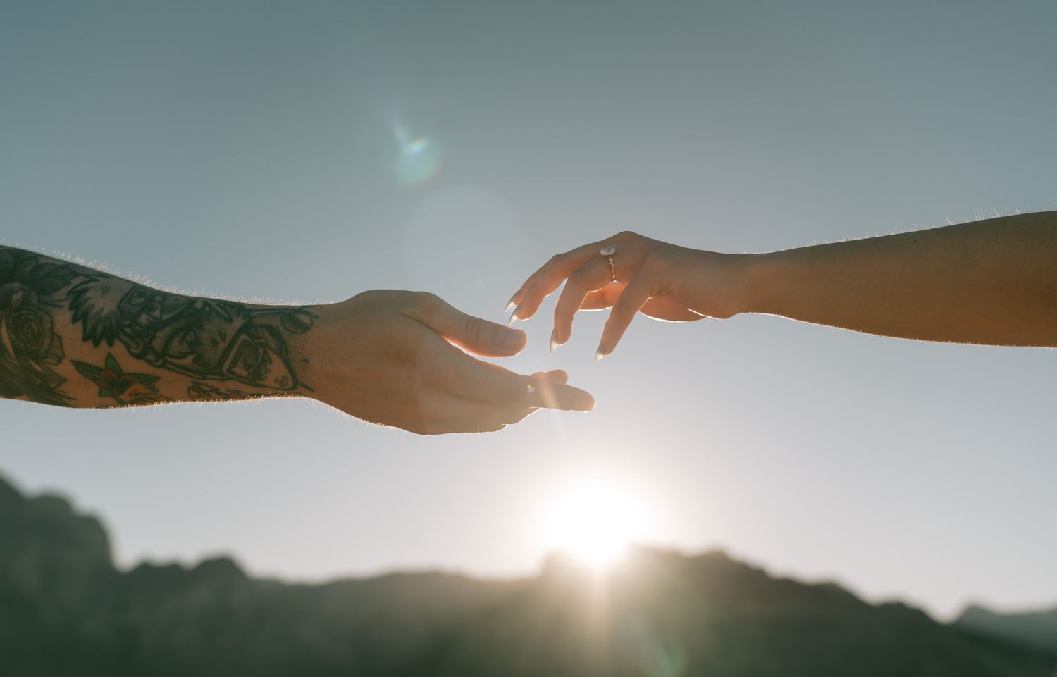 Two silhouetted hands reach toward each other against a bright sunlit sky between mountains in distance in red rock canyon, las vegas, nv.