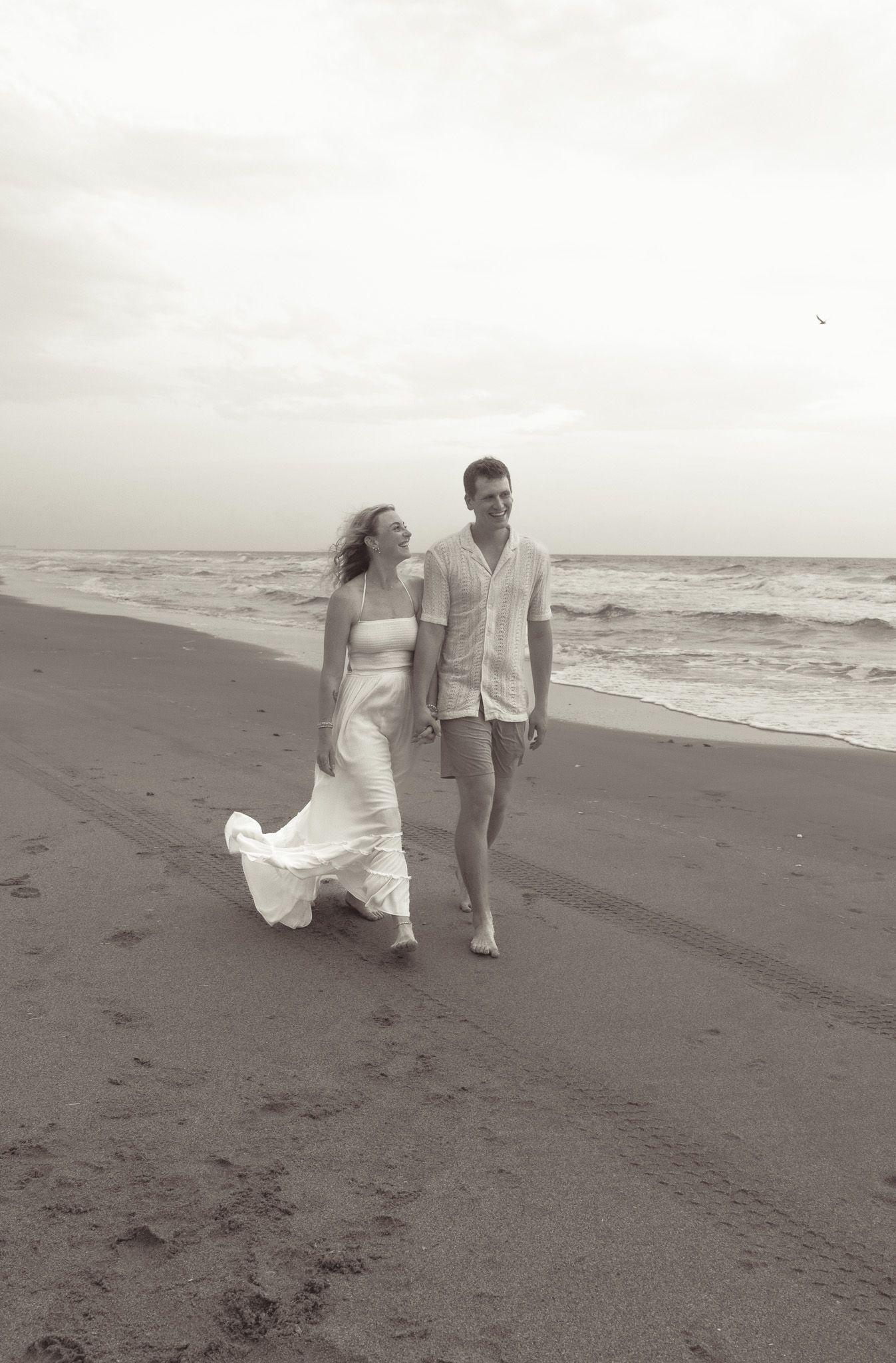 Couple walking barefoot along beach shore in black and white photography.